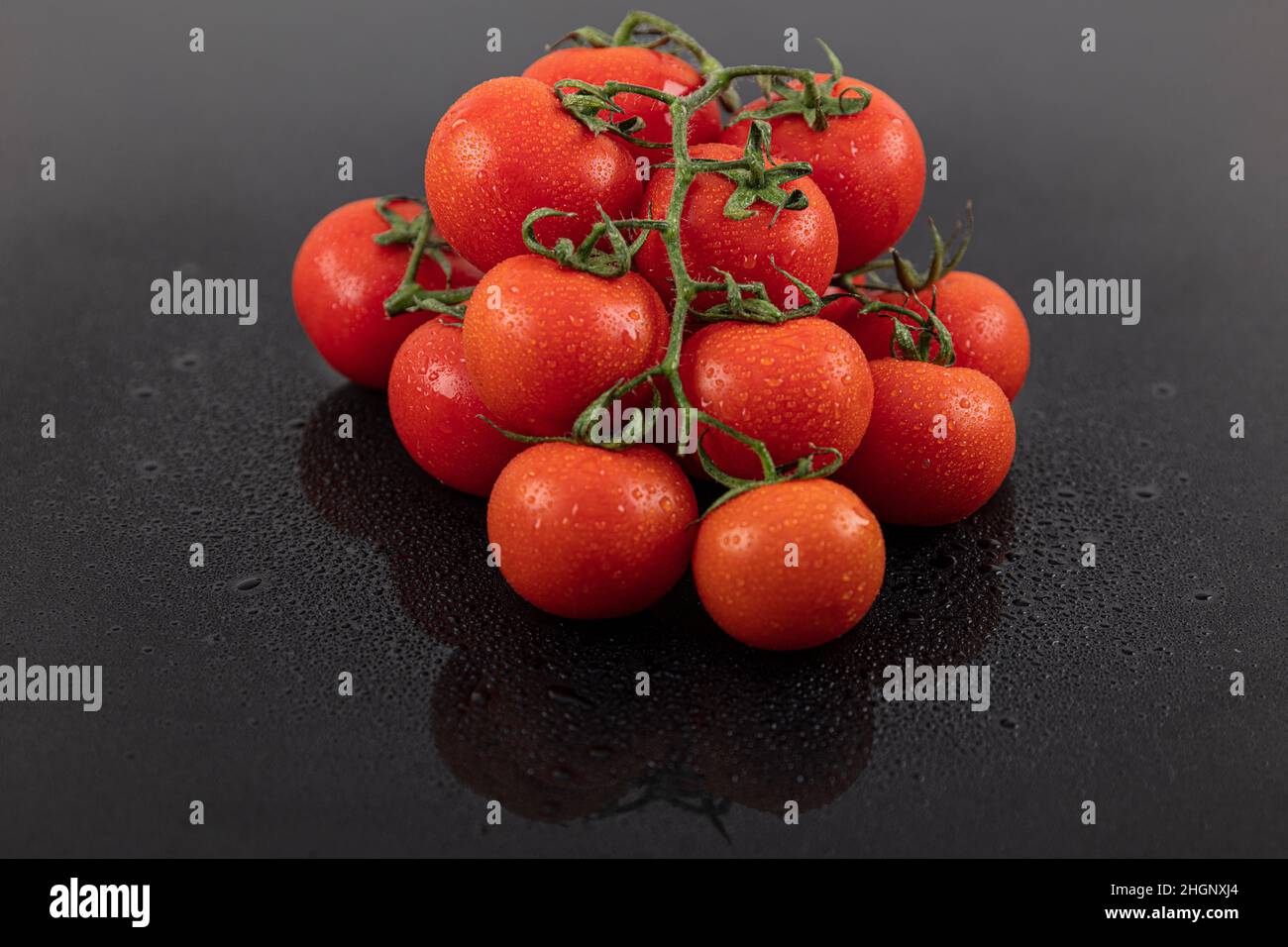 Schöne frische Weintomaten (Kirsche) mit Tropfen Wasser, roh, ganz und halbiert. Auf schwarzem texturierten Schieferhintergrund. Zutaten des Mediterranea Stockfoto