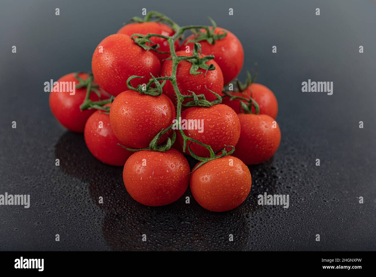 Schöne frische Weintomaten (Kirsche) mit Tropfen Wasser, roh, ganz und halbiert. Auf schwarzem texturierten Schieferhintergrund. Zutaten des Mediterranea Stockfoto