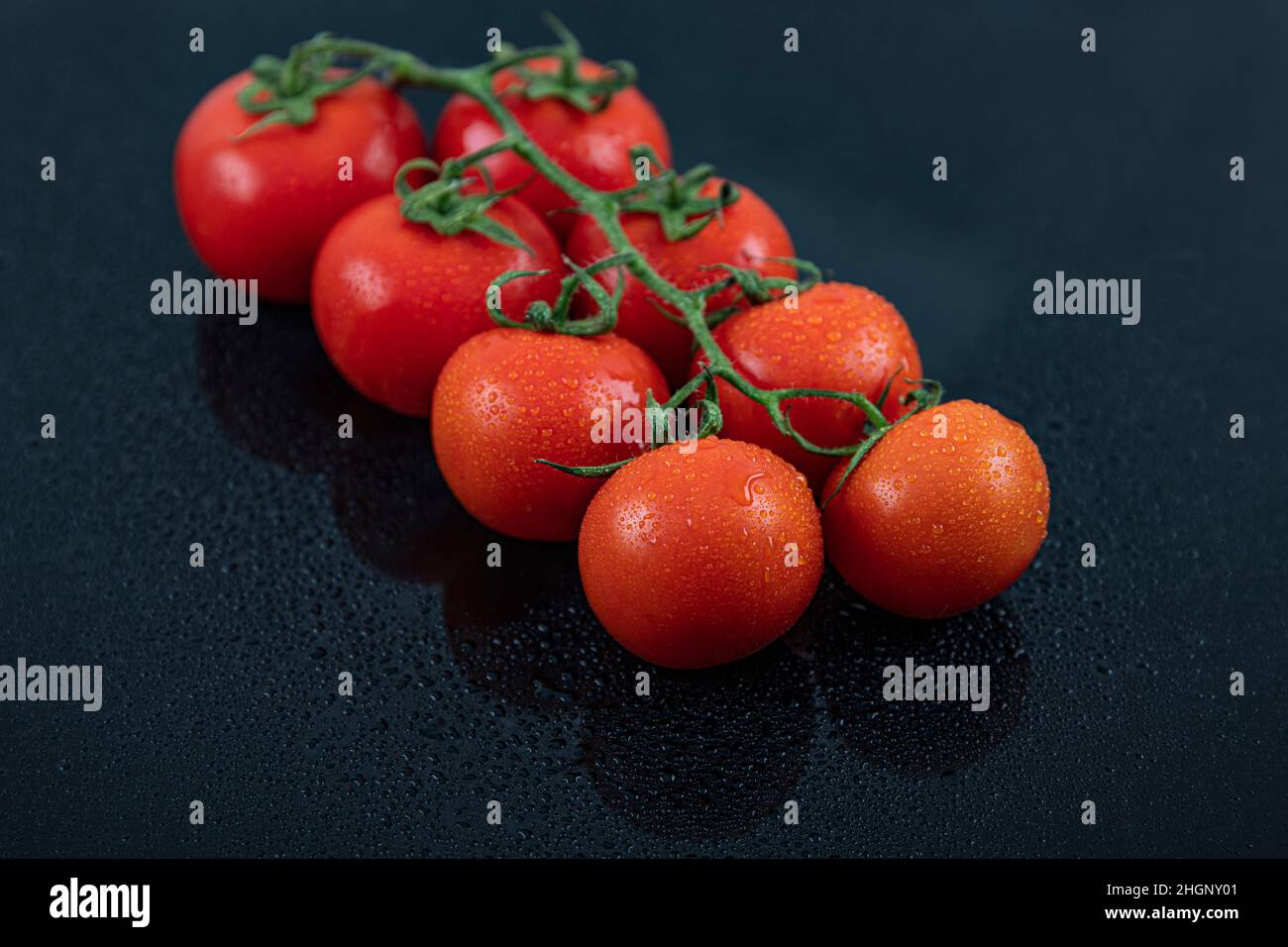 Schöne frische Weintomaten (Kirsche) mit Tropfen Wasser, roh, ganz und halbiert. Auf schwarzem texturierten Schieferhintergrund. Zutaten des Mediterranea Stockfoto