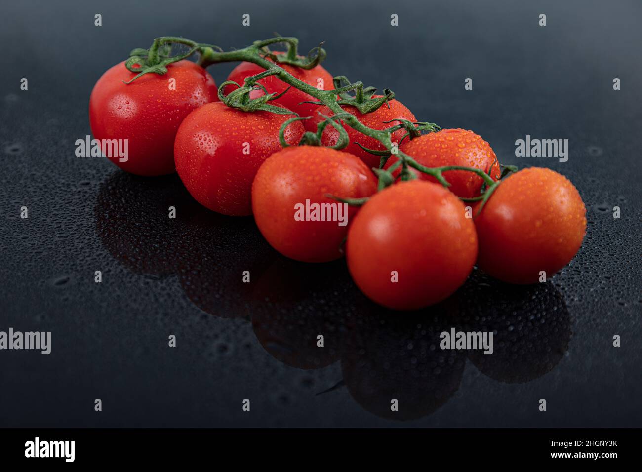 Schöne frische Weintomaten (Kirsche) mit Tropfen Wasser, roh, ganz und halbiert. Auf schwarzem texturierten Schieferhintergrund. Zutaten des Mediterranea Stockfoto