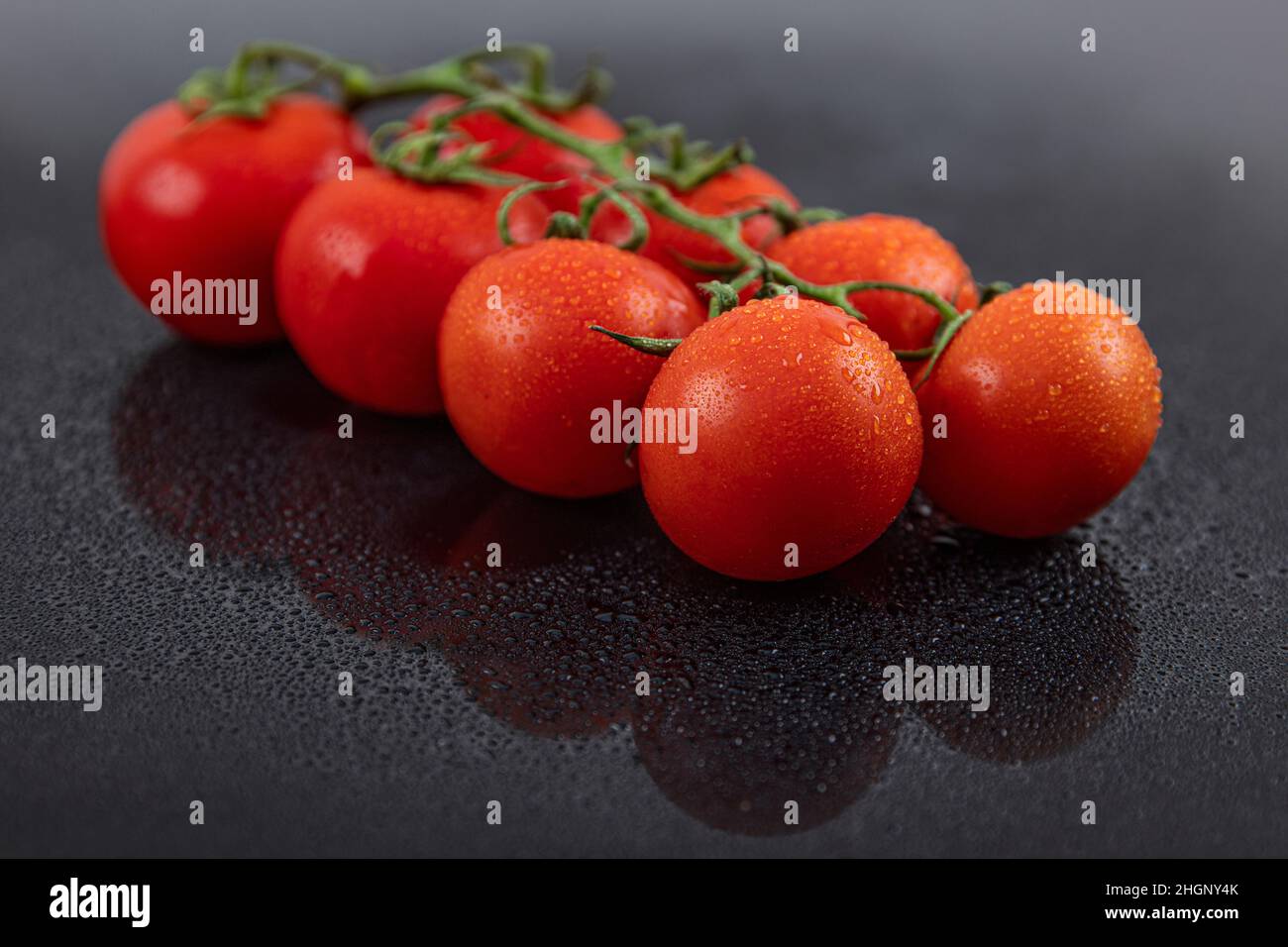 Schöne frische Weintomaten (Kirsche) mit Tropfen Wasser, roh, ganz und halbiert. Auf schwarzem texturierten Schieferhintergrund. Zutaten des Mediterranea Stockfoto