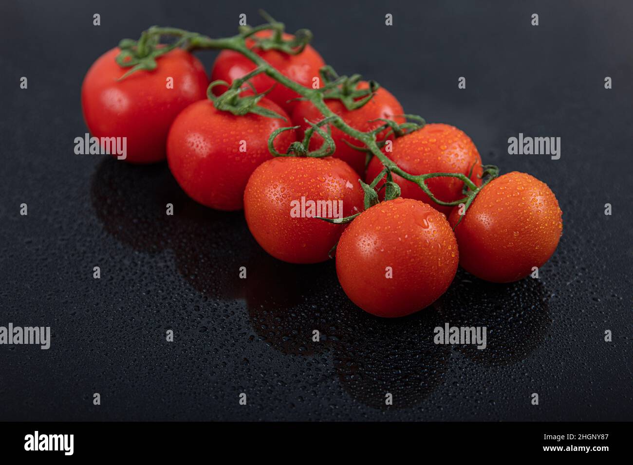 Schöne frische Weintomaten (Kirsche) mit Tropfen Wasser, roh, ganz und halbiert. Auf schwarzem texturierten Schieferhintergrund. Zutaten des Mediterranea Stockfoto
