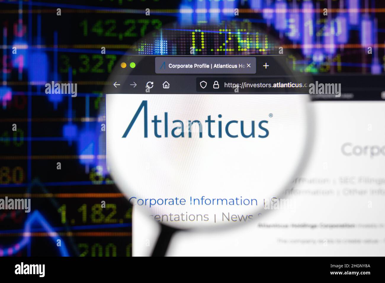 Atlanticus Firmenlogo auf einer Website mit verschwommenen Börsenentwicklungen im Hintergrund, auf einem Computerbildschirm durch eine Lupe gesehen. Stockfoto