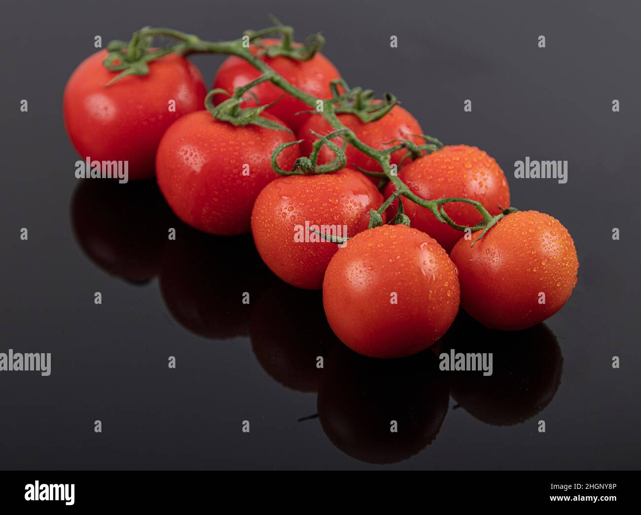 Schöne frische Weintomaten (Kirsche) mit Tropfen Wasser, roh, ganz und halbiert. Auf schwarzem texturierten Schieferhintergrund. Zutaten des Mediterranea Stockfoto