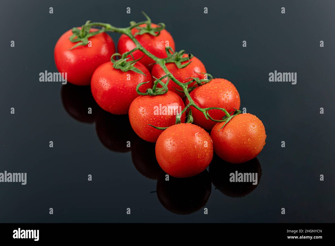 Schöne frische Weintomaten (Kirsche) mit Tropfen Wasser, roh, ganz und halbiert. Auf schwarzem texturierten Schieferhintergrund. Zutaten des Mediterranea Stockfoto