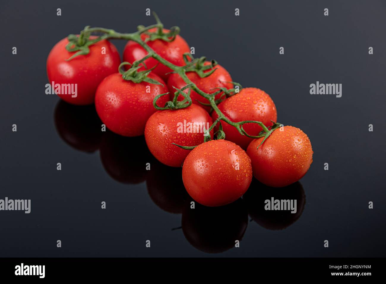 Schöne frische Weintomaten (Kirsche) mit Tropfen Wasser, roh, ganz und halbiert. Auf schwarzem texturierten Schieferhintergrund. Zutaten des Mediterranea Stockfoto