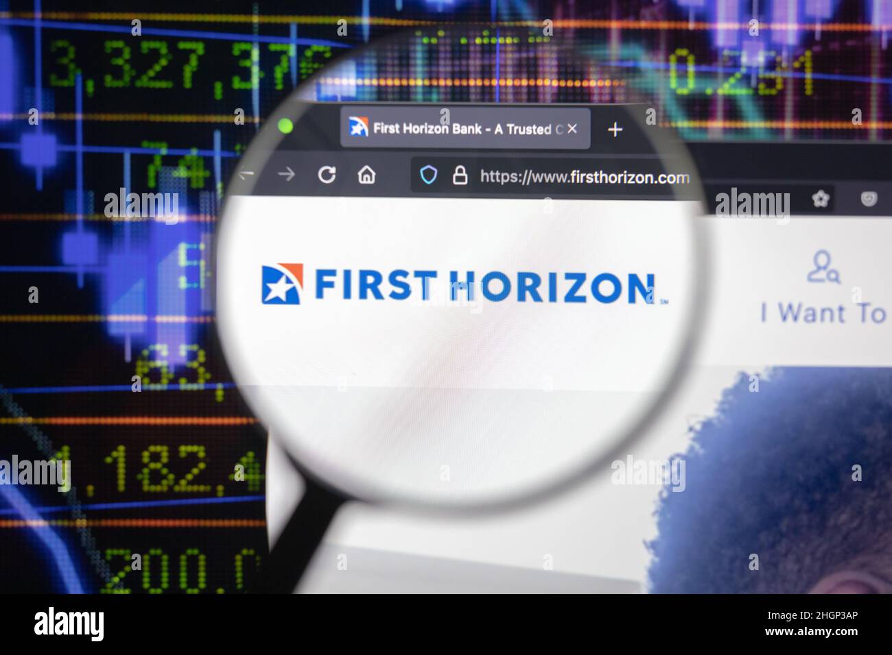 Erstes Horizon-Firmenlogo auf einer Website mit verschwommenen Börsenentwicklungen im Hintergrund, auf einem Computerbildschirm durch eine Lupe gesehen. Stockfoto