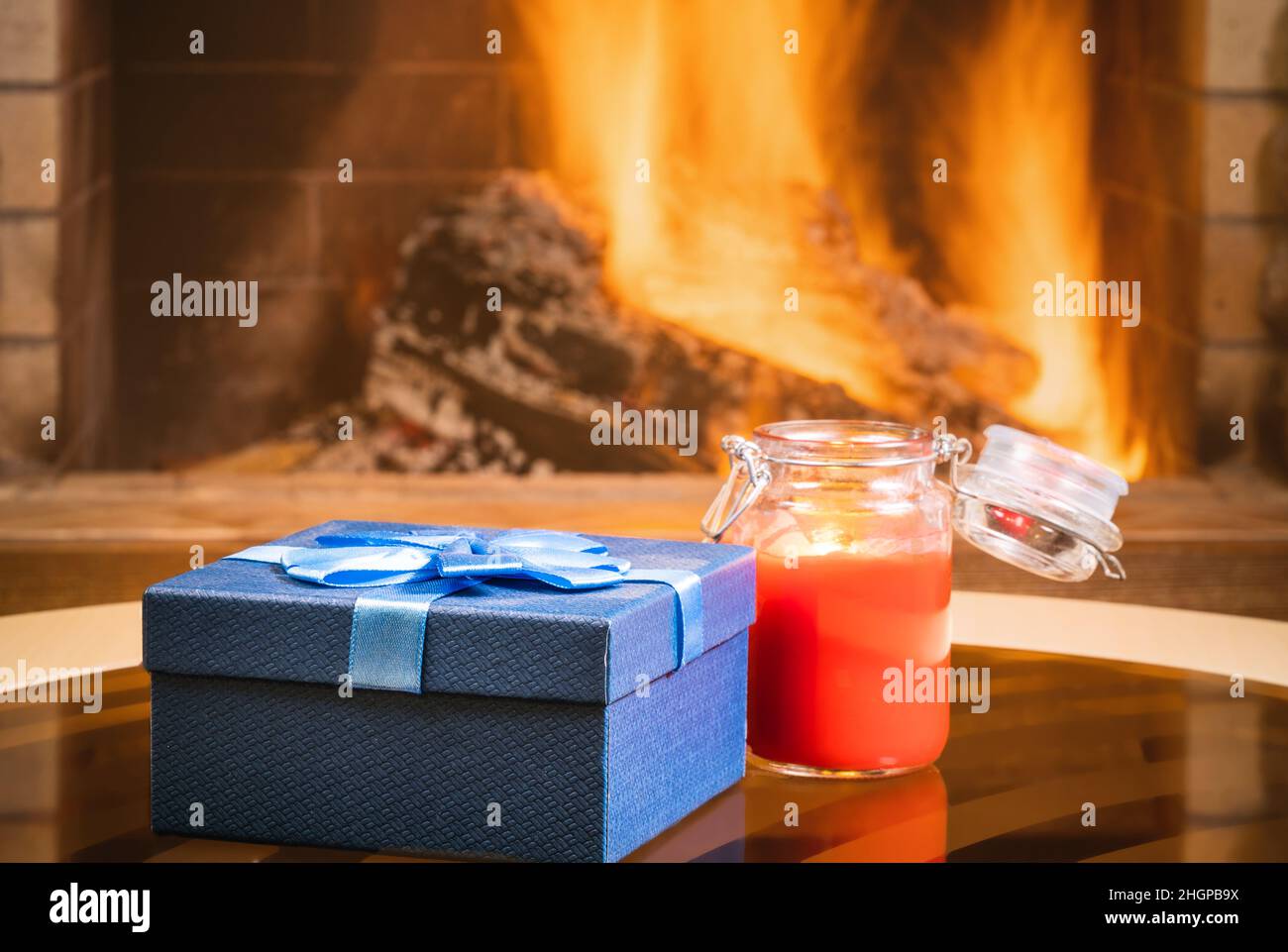 Weihnachts-Geschenkbox und Kerze in der Nähe des gemütlichen Kamins, im Landhaus. Stockfoto