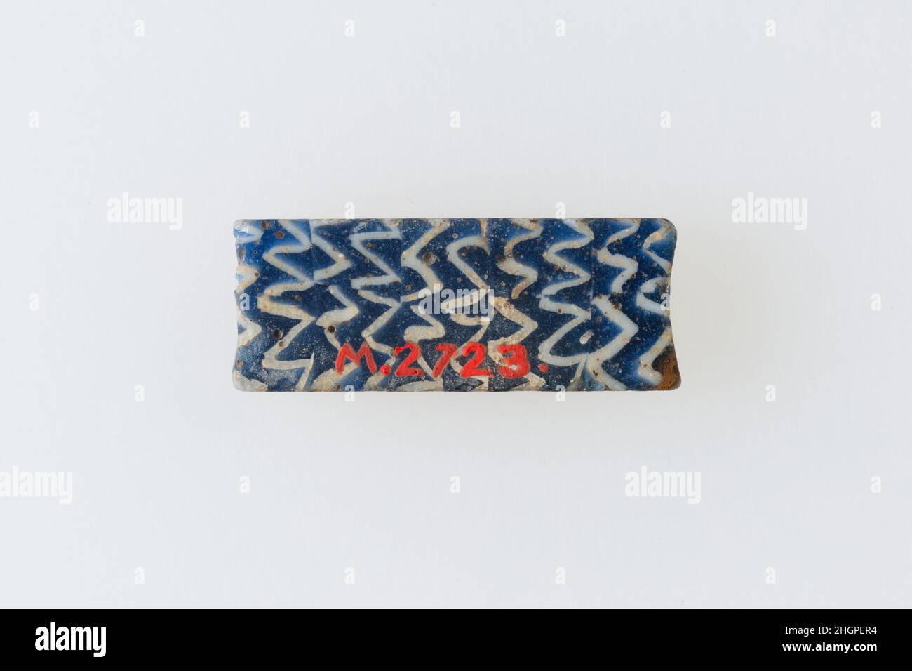 Inlay-Fragment, Reihen von Zickzacklinien 200 v. Chr.–100 n. Chr. ptolemäische Periode–Römische Periode Eine Mosaikglastechnik erlaubte die Erstellung von Vielfachen eines Bildes: Eine figürliche oder gestalterische Komposition wurde durch Bündelung von farbigen Glasstöcken hergestellt, die dann zu einem langen Balken herausgezogen wurden. Die Stange wurde dann im rechten Winkel geschnitten, wahrscheinlich durch Aufschlagen der Stange mit geeigneten Werkzeugen, um kleine Inlay-Fliesen zu produzieren. Die Fliese würde dann geglättet und auf dem Gesicht poliert, das nach außen erscheinen soll. Inlay-Fragment, Reihen von Zickzacklinien. 200 V. CHR.–100 N. CHR. Glas. Ptolemäische Periode–Römische Periode. Aus Ägypten Stockfoto