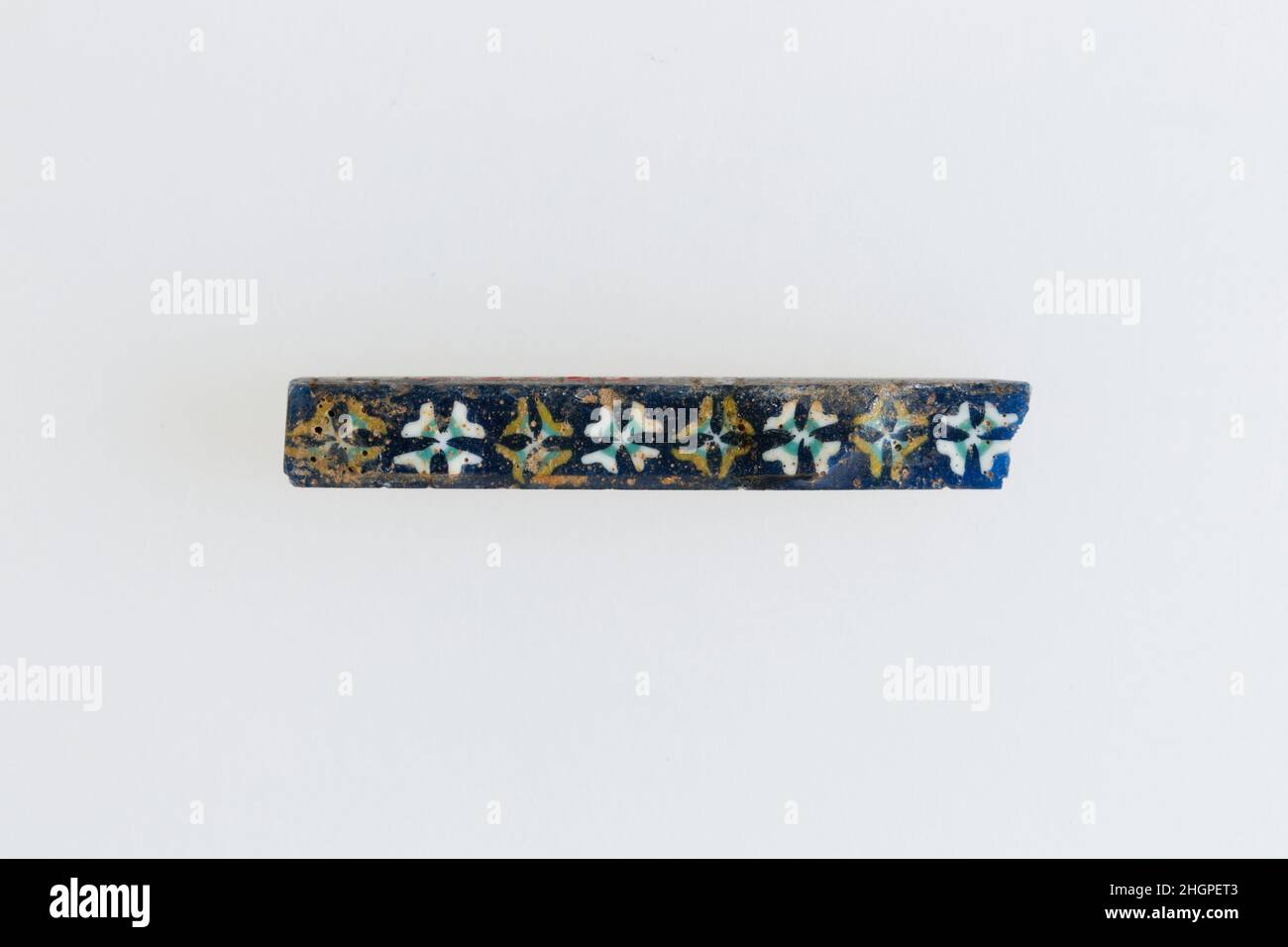 Inlay mit Rosettenreihe 200 v. Chr.–100 n. Chr. Ptolemäische Periode–Römische Periode Eine Mosaikglastechnik ermöglichte die Erstellung von Vielfachen eines Bildes: Eine figürliche oder gestalterische Komposition wurde durch Bündelung von farbigen Glasstöcken hergestellt, die dann zu einem langen Balken herausgezogen wurden. Die Stange wurde dann im rechten Winkel geschnitten, wahrscheinlich durch Aufschlagen der Stange mit geeigneten Werkzeugen, um kleine Inlay-Fliesen zu produzieren. Die Fliese würde dann geglättet und auf dem Gesicht poliert, das nach außen erscheinen soll.solche Elemente könnten auch nebeneinander verwendet werden, um sich wiederholende Muster zu erstellen. Inlay mit einer Reihe von Rosetten. 200 V. CHR.–100 N. CHR. Glas. Zapfwelle Stockfoto