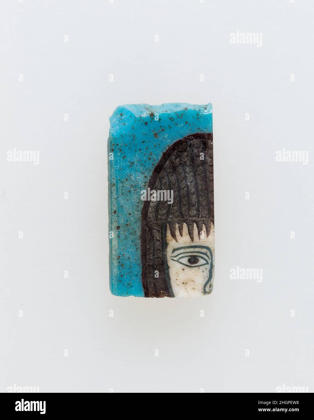 Inlay, Teil des Kopfes 100 v. Chr.–100 n. Chr. Ptolemäische Periode–Römische Periode Eine Mosaikglas-Technik ermöglichte die Schaffung von Vielfachen eines Bildes: Eine figürliche oder gestalterische Komposition wurde durch Bündelung von farbigen Glasstöcken hergestellt, die dann zu einem langen Balken herausgezogen wurden. Die Stange wurde dann im rechten Winkel geschnitten, wahrscheinlich durch Aufschlagen der Stange mit geeigneten Werkzeugen, um kleine Inlay-Fliesen zu produzieren. Die Fliese würde dann geglättet und auf dem Gesicht poliert, das nach außen erscheinen soll.solche Elemente könnten auch nebeneinander verwendet werden, um sich wiederholende Muster zu erstellen. Oder wenn die Stange eine Hälfte eines Elements darstellte, das symme war Stockfoto