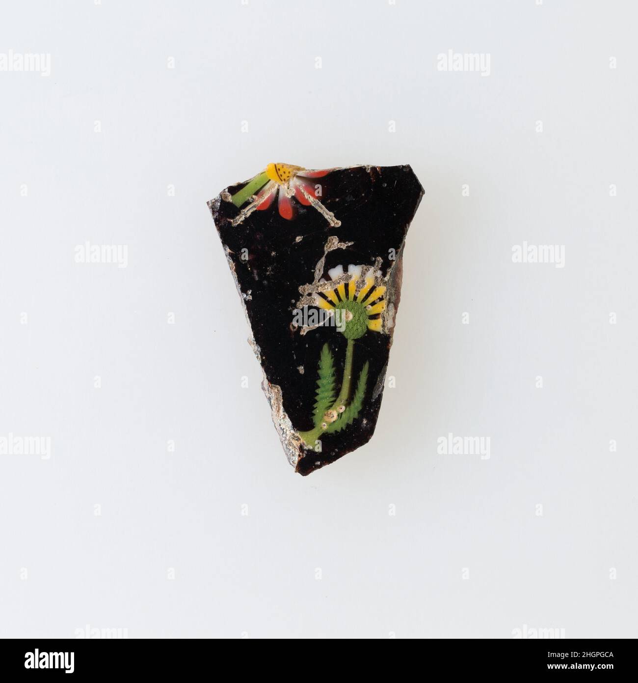 Florale Plakette 100 v. Chr.–100 n. Chr. ptolemäische Periode–Römische Zeit Eine Mosaikglastechnik ermöglichte die Erstellung von Vielfachen eines Bildes: Eine figürliche oder gestalterische Komposition wurde durch die Bündelung von farbigen Glasstöcken hergestellt, die dann zu einer langen Stange herausgezogen wurden. Die Stange wurde dann im rechten Winkel geschnitten, wahrscheinlich durch Aufschlagen der Stange mit geeigneten Werkzeugen, um kleine Inlay-Fliesen zu produzieren. Die Fliese würde dann geglättet und auf dem Gesicht poliert, das nach außen erscheinen soll. Solche Elemente könnten auch nebeneinander verwendet werden, um sich wiederholende Muster zu erzeugen. Oder wenn der Stab eine Hälfte eines Elements darstellte, das symmetrisch war Stockfoto