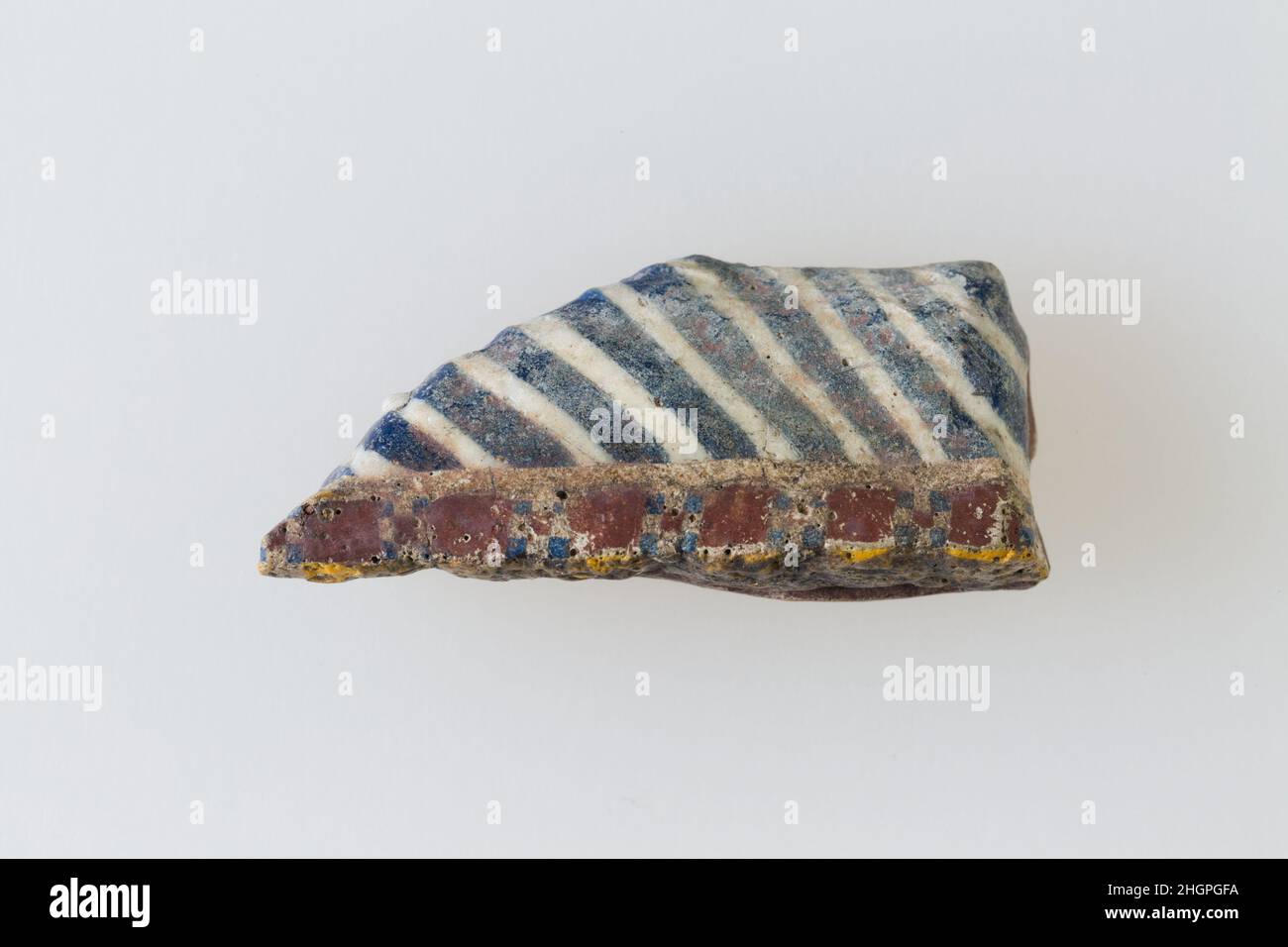 Einlage mit Streifen 200 v. Chr.–100 n. Chr. Ptolemäische Periode–Römische Zeit Eine Mosaikglastechnik ermöglichte die Erstellung von Vielfachen eines Bildes: Eine figürliche oder gestalterische Komposition wurde durch Bündelung von farbigen Glasstöcken hergestellt, die dann zu einem langen Balken herausgezogen wurden. Die Stange wurde dann im rechten Winkel geschnitten, wahrscheinlich durch Aufschlagen der Stange mit geeigneten Werkzeugen, um kleine Inlay-Fliesen zu produzieren. Die Fliese würde dann geglättet und auf dem Gesicht poliert, das nach außen erscheinen soll. Einlage mit Streifen. 200 V. CHR.–100 N. CHR. Glas. Ptolemäische Periode–Römische Periode. Aus Ägypten Stockfoto