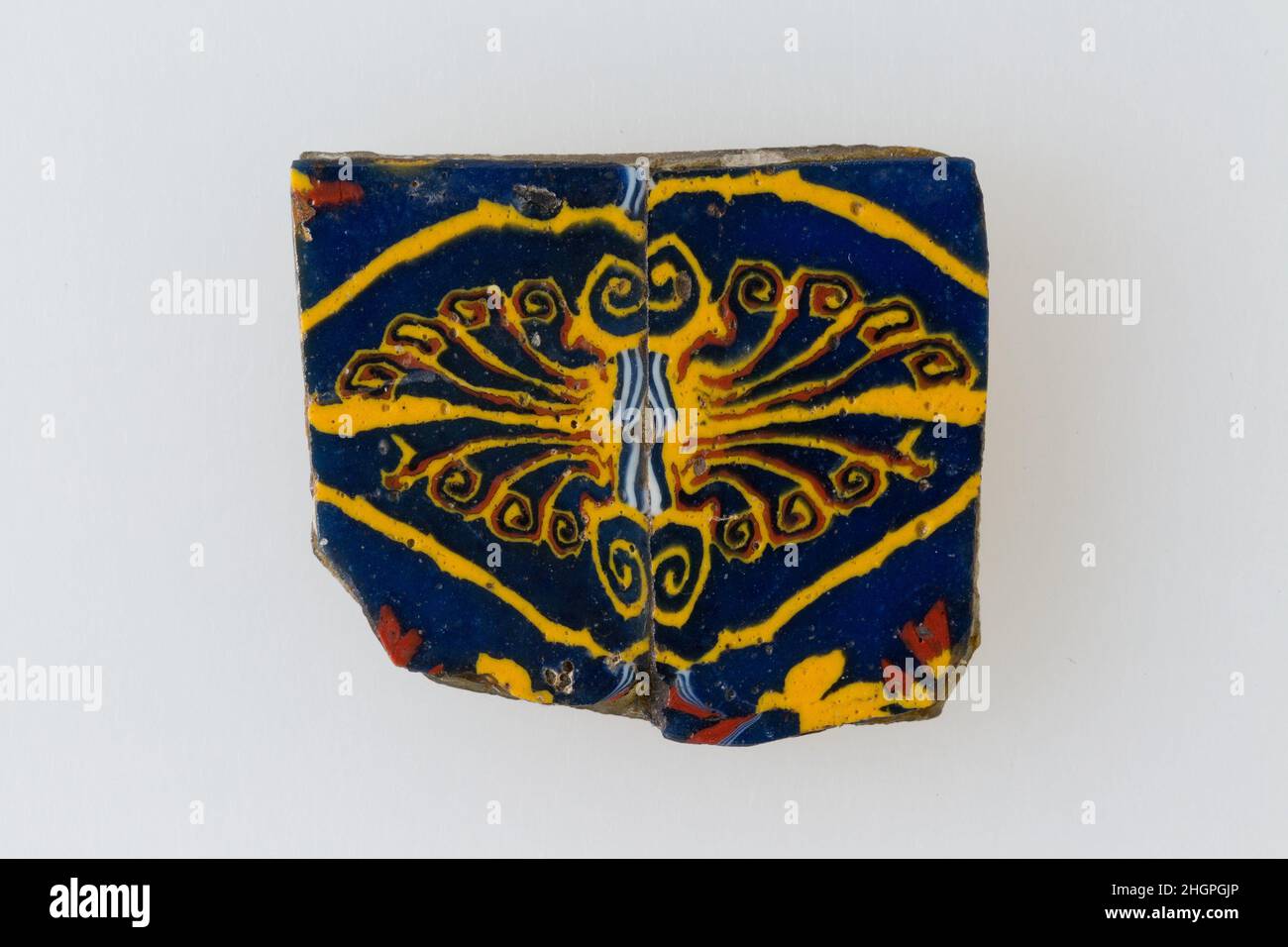 Inlay, palmette 100 v. Chr.–100 n. Chr. Ptolemäische Periode–Römische Zeit Eine Mosaikglastechnik ermöglichte die Erstellung von Vielfachen eines Bildes: Eine figürliche oder gestalterische Komposition wurde durch Bündelung von farbigen Glasstöcken hergestellt, die dann zu einem langen Balken herausgezogen wurden. Die Stange wurde dann im rechten Winkel geschnitten, wahrscheinlich durch Aufschlagen der Stange mit geeigneten Werkzeugen, um kleine Inlay-Fliesen zu produzieren. Die Fliese würde dann geglättet und auf dem Gesicht poliert, das nach außen erscheinen soll. Inlay, Palmette. 100 V. CHR.–100 N. CHR. Glas. Ptolemäische Periode–Römische Periode. Aus Ägypten Stockfoto