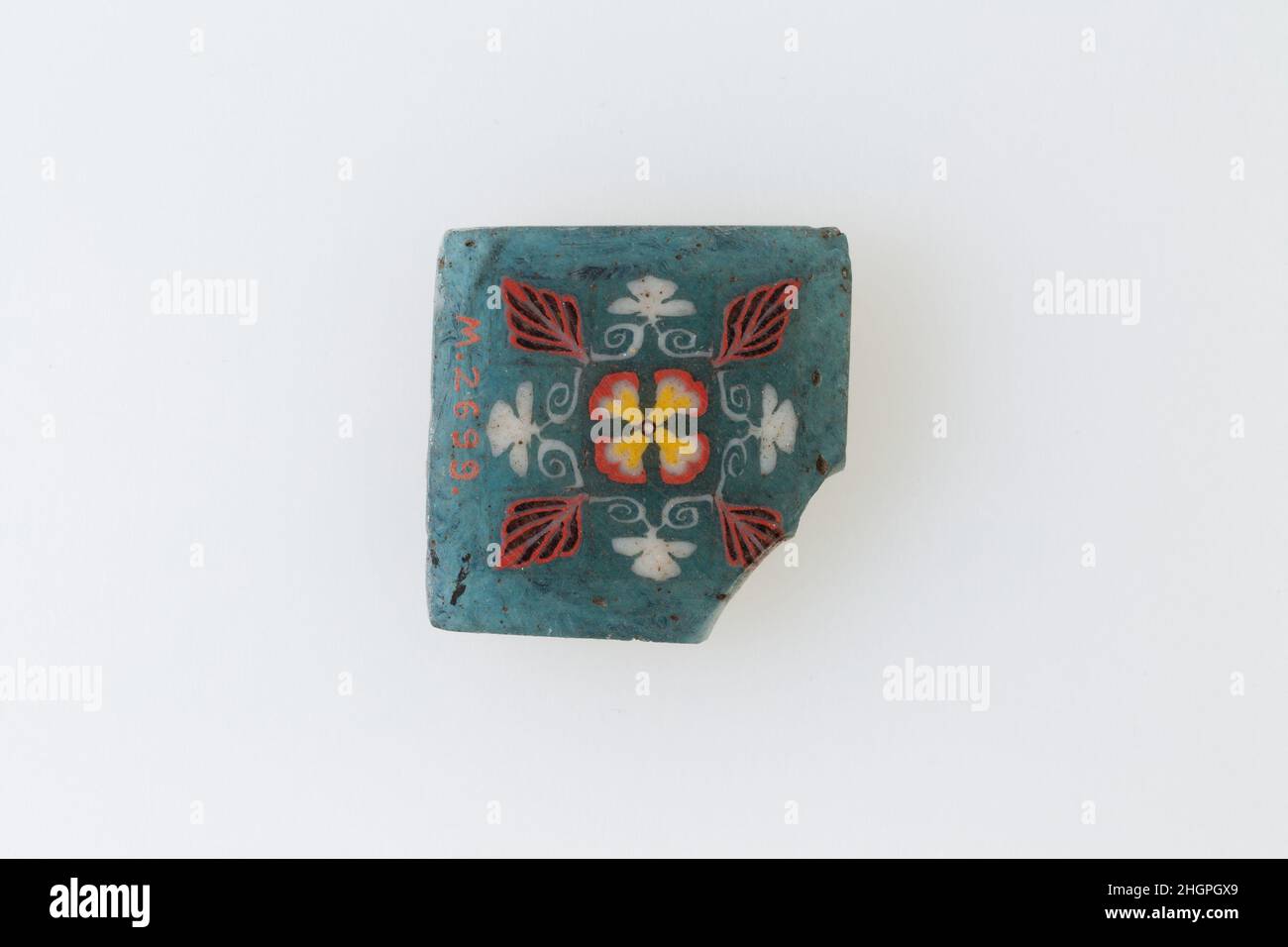 Einlage, florales Quadrat 1st–3rd Jahrhundert n. Chr. Römische Periode Eine Mosaikglastechnik ermöglichte die Schaffung von Vielfachen eines Bildes: Eine figürliche oder gestalterische Komposition wurde durch die Bündelung von farbigen Glasstöcken hergestellt, die dann zu einer langen Stange herausgezogen wurden. Die Stange wurde dann im rechten Winkel geschnitten, wahrscheinlich durch Aufschlagen der Stange mit geeigneten Werkzeugen, um kleine Inlay-Fliesen zu produzieren. Die Fliese würde dann geglättet und auf dem Gesicht poliert, das nach außen erscheinen soll. Einlage, quadratisch mit Blumenmuster. 1st–3rd Jahrhundert n. Chr. Mosaikglas. Römische Zeit. Aus Ägypten Stockfoto
