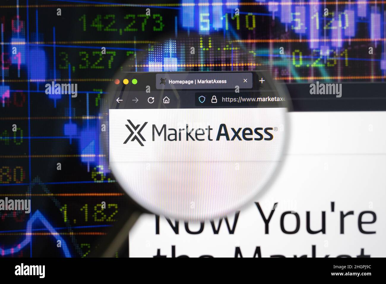 Market Axss Firmenlogo auf einer Website mit verschwommenen Börsenentwicklungen im Hintergrund, auf einem Computerbildschirm durch eine Lupe gesehen. Stockfoto