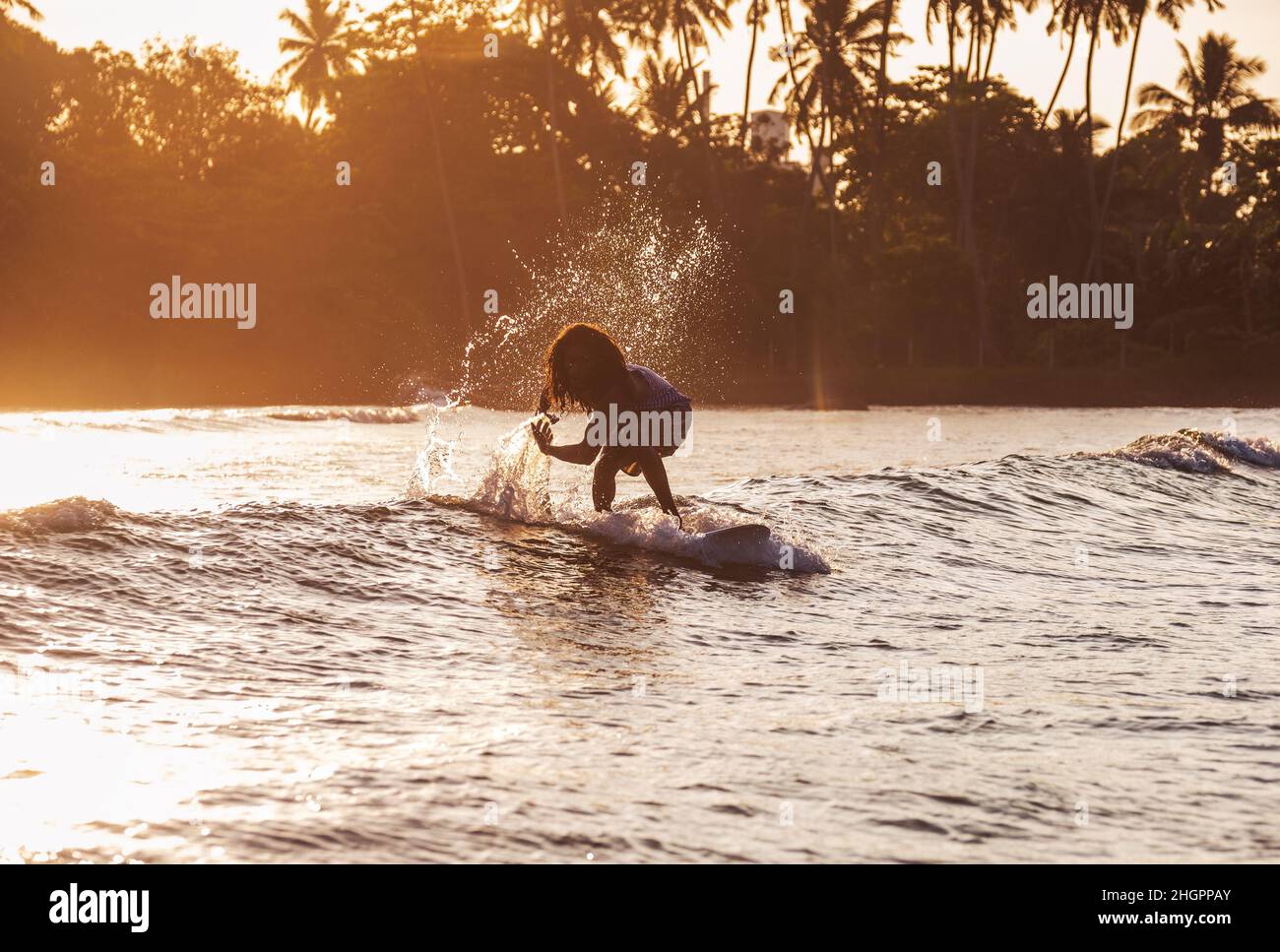 Schwarze langhaarige Teenager junge Silhouette Reiten ein langes Surfbrett. Er fing eine Welle in einer Bucht des indischen Ozeans mit magischem Sonnenuntergang Hintergrund. Extreme Wasser sp Stockfoto