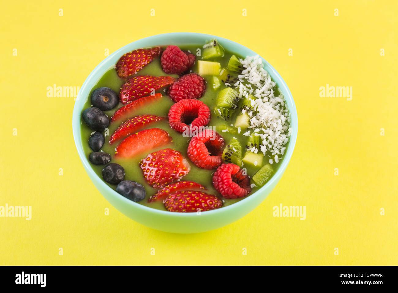 Smoothie Schüssel mit frischen Beeren und Früchten in blauer Platte auf gelb Stockfoto