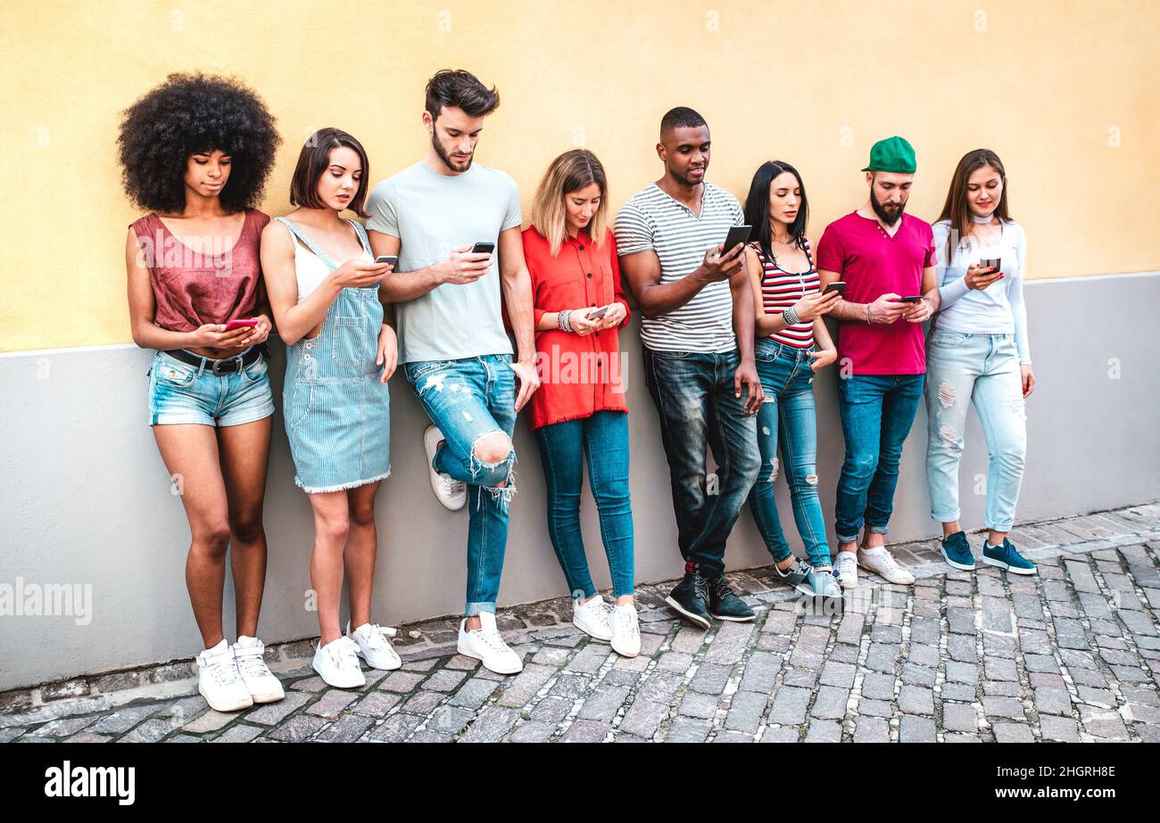 Multikulturelle Milenials mit Smartphone gegen die Wand im Garten der Uni - Junge Studenten süchtig nach Handy Stockfoto