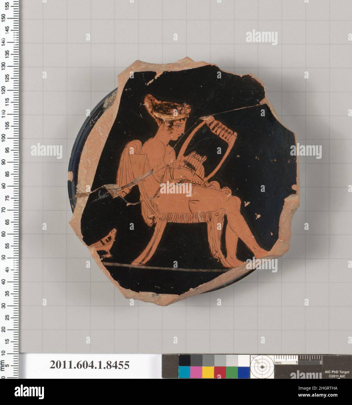 Terracotta-Fragment einer stammlosen Kylix (Trinkbecher) Mitte des 5th. Jahrhunderts v. Chr. Griechisch, Dachboden, auf einem Exergue, Frau, die auf einem Draperie nach rechts saß, einen Kranz und ein Band in den Haaren trug, sowie ein Oberschenkelband und Armbänder, Mit einer Leier in der linken Hand und einem Plektron in der rechten Hand; auf dem Boden ein Vogel; außen profilierter Ringfuß, Mit einer verglasten Ruheplatte; die Innenwand des Fußes ist ebenfalls glasiert; die Unterseite des Fußbodens ist mit konzentrischen Kreisen verziert; der äußere Ring ist in Reserve, gefolgt von einem breiten Band aus schwarzer Glasur, einem dünnen Band aus Reserve und einem dünnen Band aus schwarzem gla Stockfoto