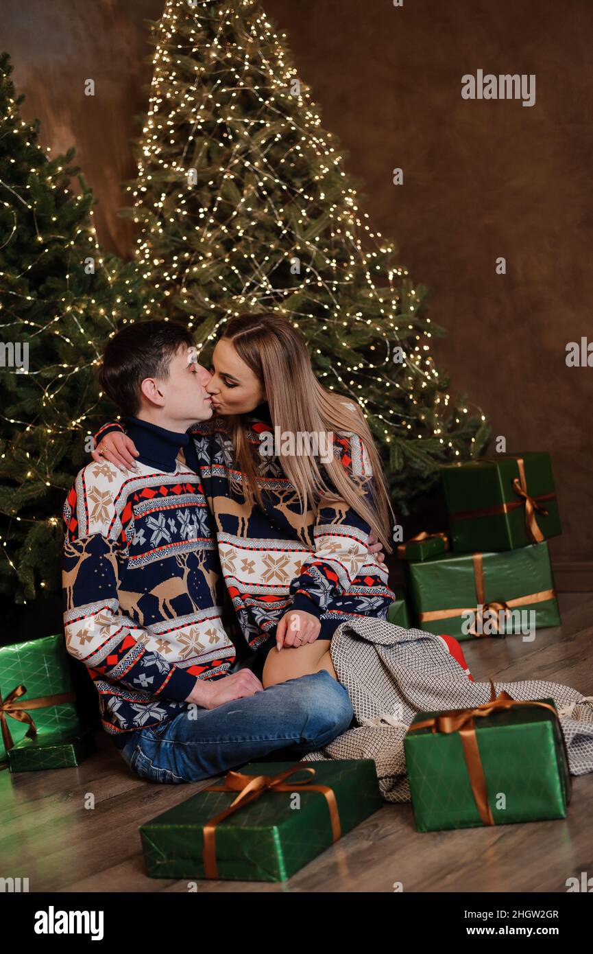 Ein Mann und ein Mädchen umarmen und küssen sich vor dem Hintergrund eines Weihnachtsbaums und eines roten Sofas Stockfoto