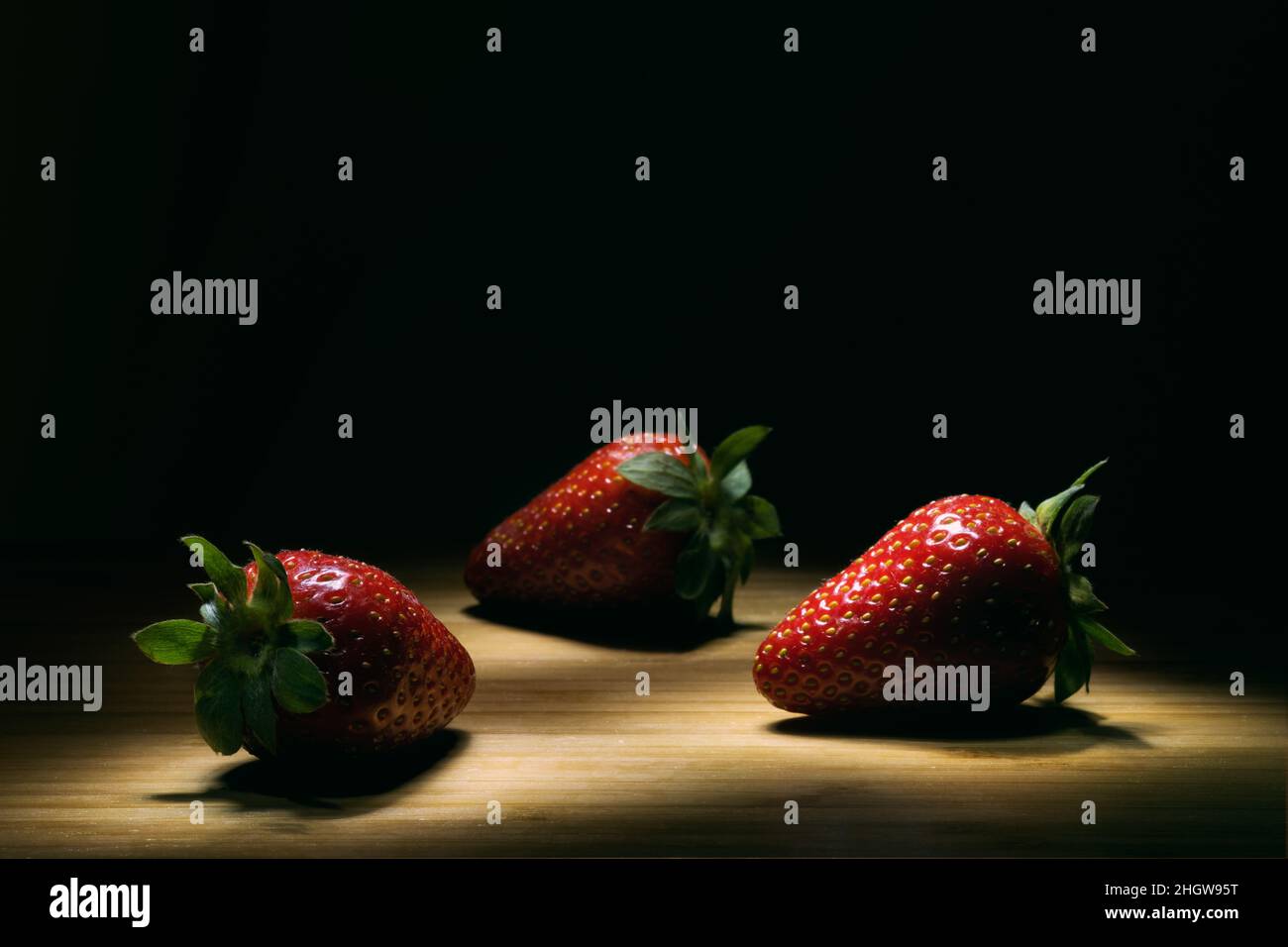 Drei Erdbeeren auf einem Holzboden mit hohem Kontrast. Stockfoto