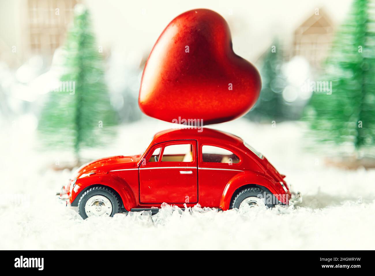 Rotes Retro-Auto mit Herz in einer Winterlandschaft. Postkarte zum Valentinstag. Urlaubslieferung. Selektiver Fokus. Stockfoto