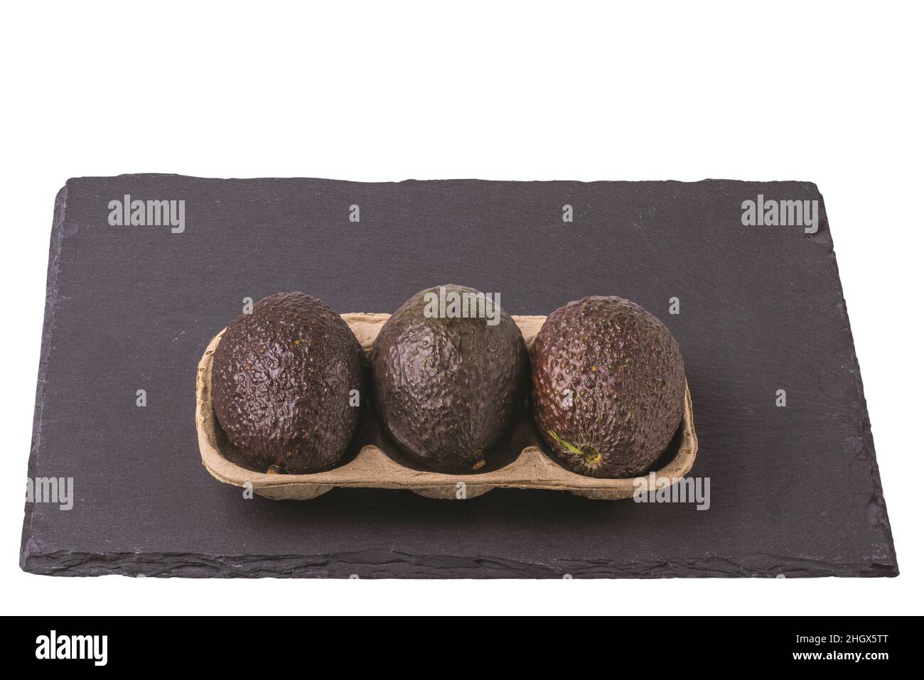 Nahaufnahme eines Avocado-Pakets, das auf einem schwarzen Felsenschneidebrett isoliert ist. Stockfoto