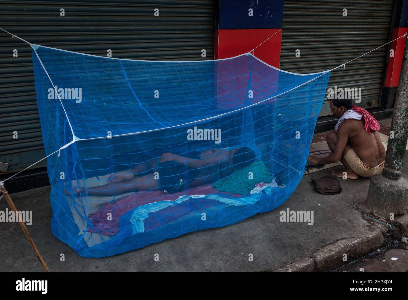 Der Mann schläft auf der Straße, die von einem Anti-Malaria-Moskitonetz geschützt ist. Kalkutta, Indien. Stockfoto