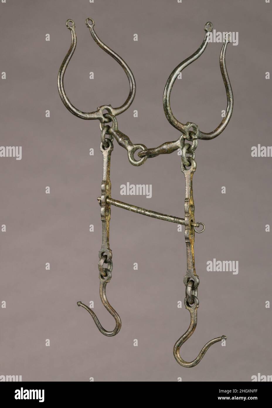 Curb Bit 2nd–1st Jahrhundert v. Chr. Thrakisch oder Ostkeltisch das Mundstück dieses Bits besteht aus zwei spindelförmigen Gliedern, die in der Mitte artikuliert sind. Sie sind auf beiden Seiten mit sehr eleganten lyerförmigen Aufsätzen für die Wangenstücke des Wadenschals verbunden. Die beiden Schäfte, an denen Haken für die Zügel hängen, sind durch einen horizontalen Stab verbunden, der als Bordstein fungiert und durch drei Perforationen in drei Positionen verstellbar ist. Die Bordsteinkante hätte das Kinn des Pferdes gedrückt, als die Zügel zurückgezogen wurden. Die großen lyrerförmigen Elemente halfen, die Richtung des Pferdes anzuzeigen und hielten die Spitze an ihrem Platz fest Stockfoto