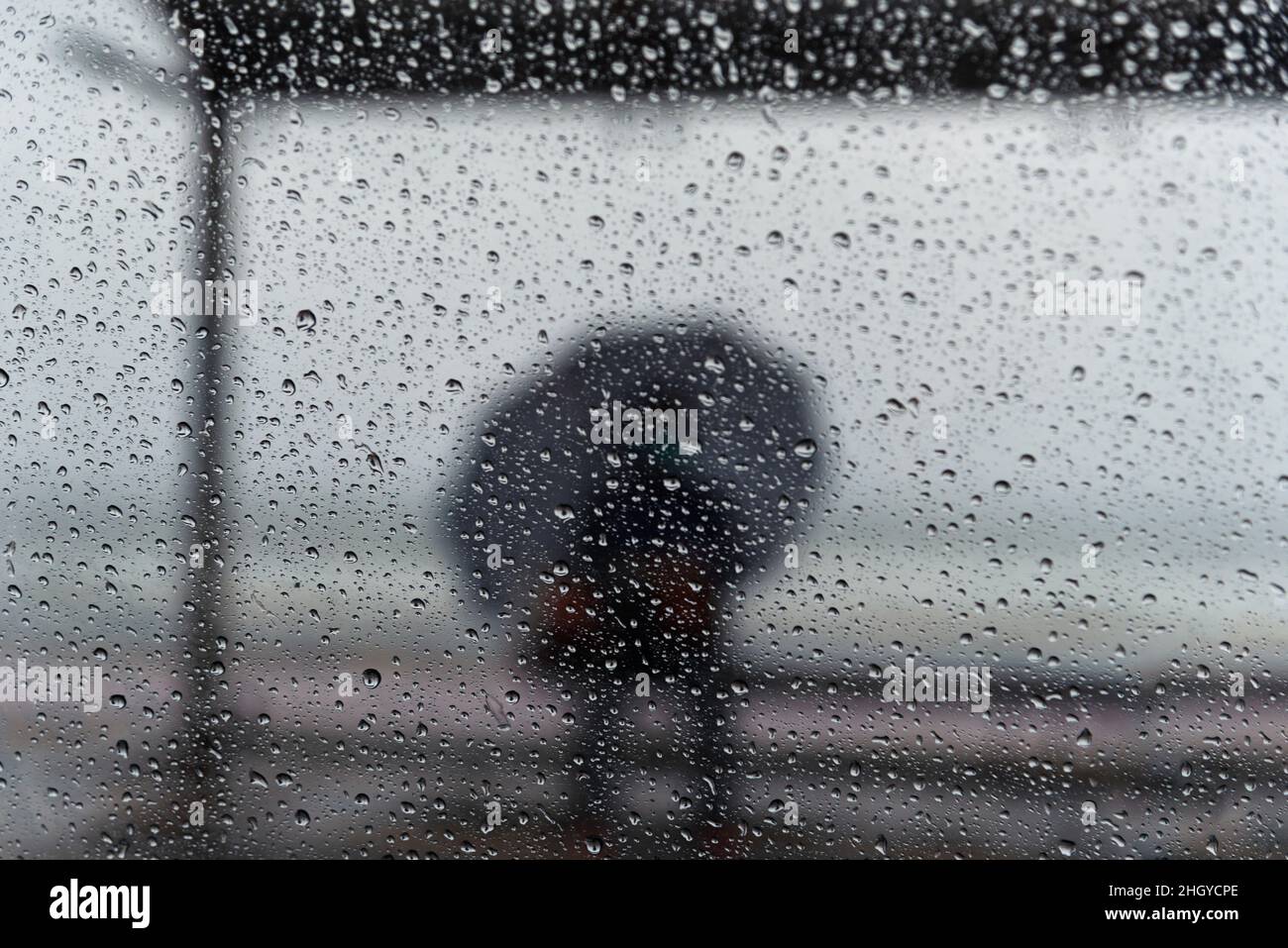 Salvador, Bahia, Brasilien - 15. November 2021: Ein Passagier sitzt an der Bushaltestelle mit einem Regenschirm. Salvador, Bahia, Brasilien. Stockfoto