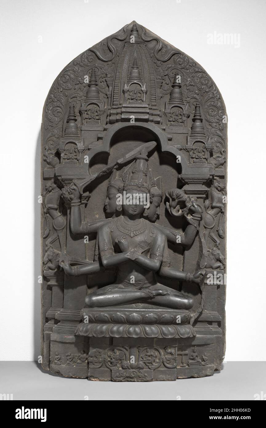 Manjuvajra Mandala 11th. Jahrhundert Bangladesch oder Indien (Bengalen) Diese Skulptur stellt eine esoterische Form von Manjushri dar, dem Bodhisattva der transzendenten Weisheit. Er hat drei Köpfe und sechs Arme; vier halten einen Pfeil und Bogen, ein Schwert und einen Lotus, während die anderen zwei Vajras (Donnerbolzenzepter) halten und in einer esoterischen Geste (Mudra), die höchste Weisheit identifiziert, an der Brust gekreuzt werden. Am prominentesten unter diesen Waffen ist das Schwert, das Unwissenheit und Täuschung abschneidet. Leogryphen, die auf Löwen stehen, umrahmen den Thronsitz; mythische Makara-Ausgabe aus dem dreigliedrigen, geknallten Nimbus; und grillen Stockfoto