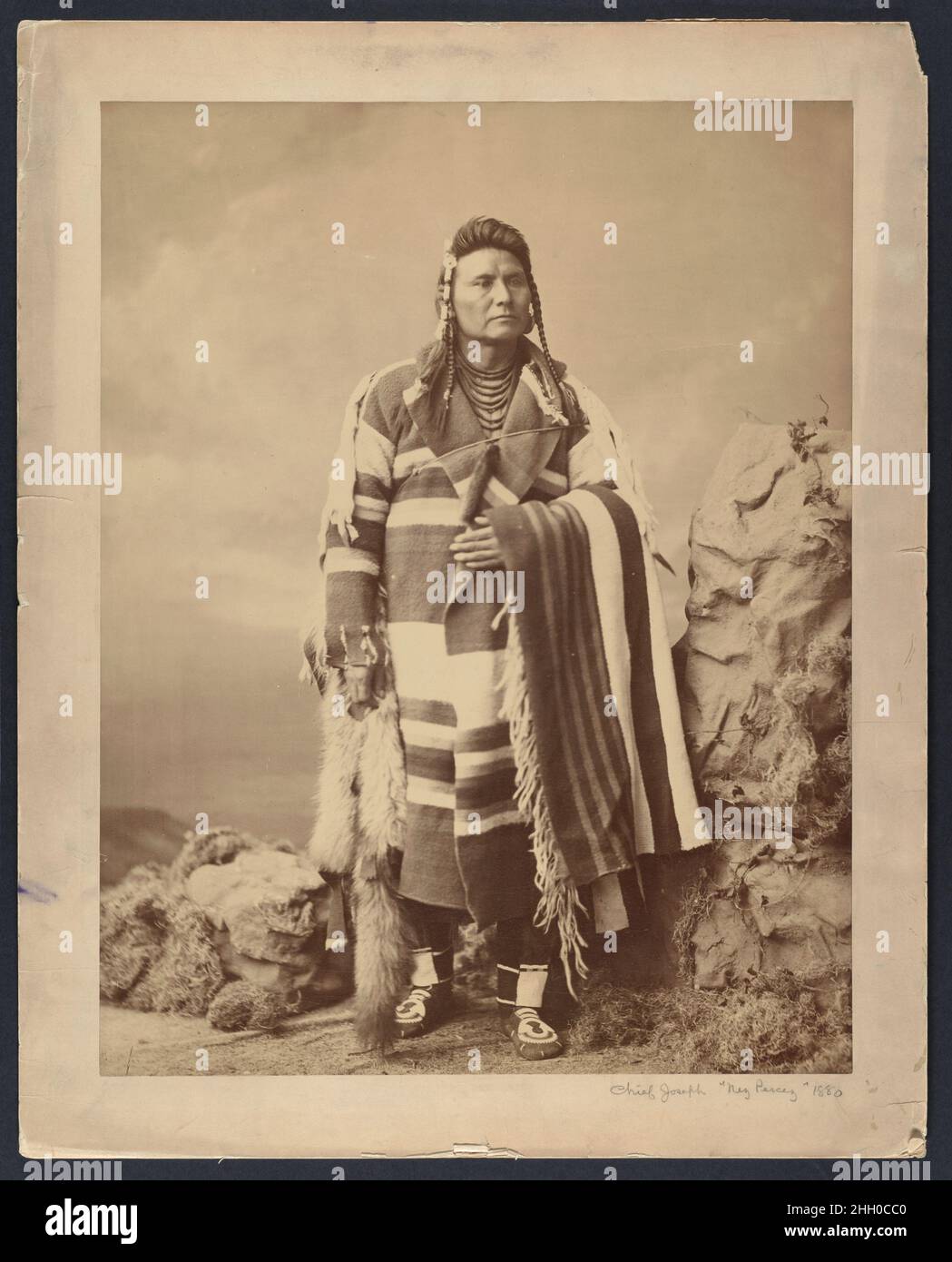 Hinmatóowyalahtq’it (Chief Joseph) 1879 Charles Milton Bell American im Jahr 1879, während er gewaltsam auf ein Reservat im heutigen Oklahoma, Hinmatóowyalahtq’it, Oder Chief Joseph durfte nach Washington, D.C., reisen, wo er sich mit Präsident Rutherford B. Hayes traf und seinen Fall für die Rückkehr der Nez Perce in den pazifischen Nordwesten vorstellte. Wie es für die einheimischen Delegierten üblich war, die die Hauptstadt besuchten, posierte er für ein fotografisches Porträt im Atelier von Bell. In einer künstlichen Landschaft, die aus einem papierenen Felsen, einem Kunstmoos und einer gemalten Kulisse besteht, blickt Chief Joseph in die mâché Stockfoto