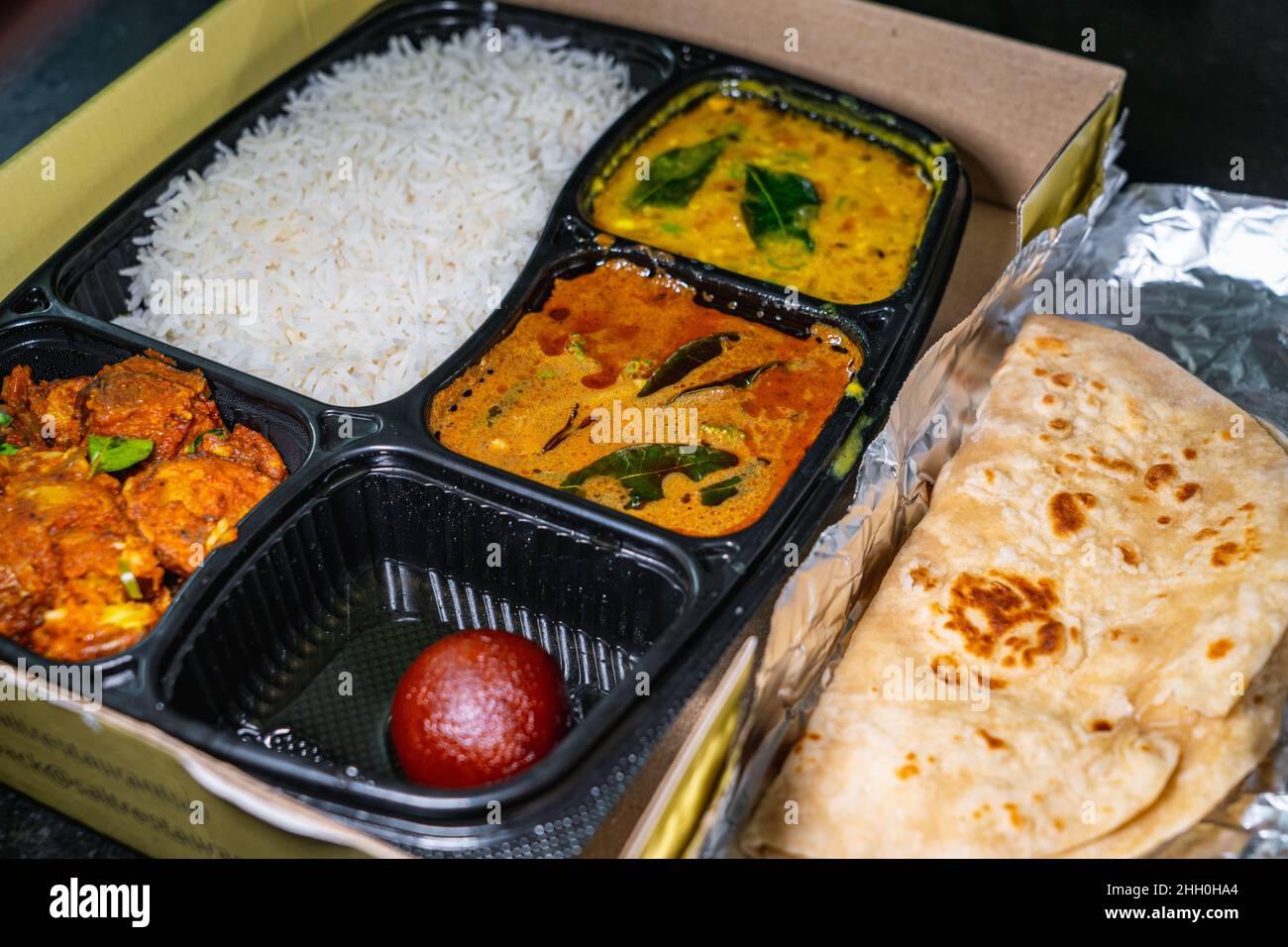 Selektiver Fokus einer Vielzahl von indischen Speisen zum Mitnehmen in einem schwarzen Plastikbehälter. Stockfoto
