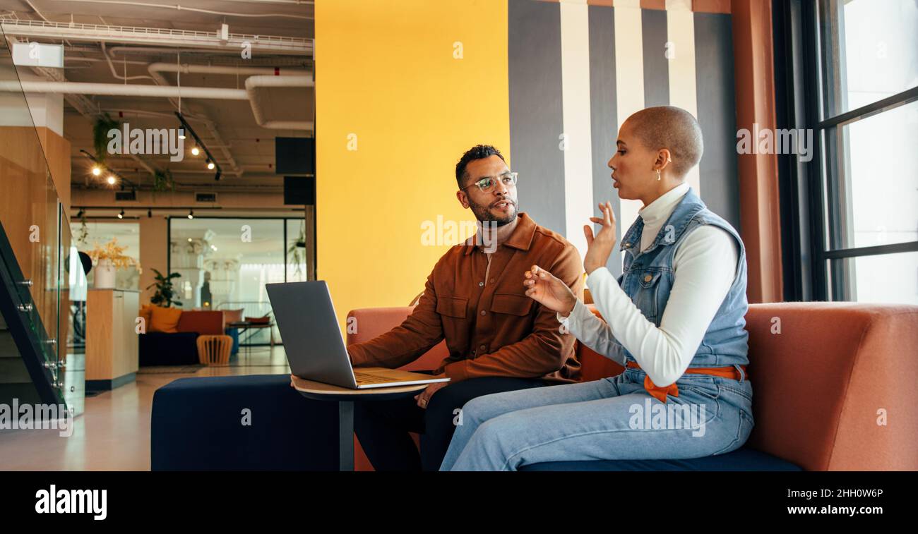 Zwei junge Geschäftsleute, die in einer Bürolobby eine wichtige Diskussion führen. Zwei junge Unternehmer arbeiten in einem Co-Working Spa an einem neuen Projekt zusammen Stockfoto