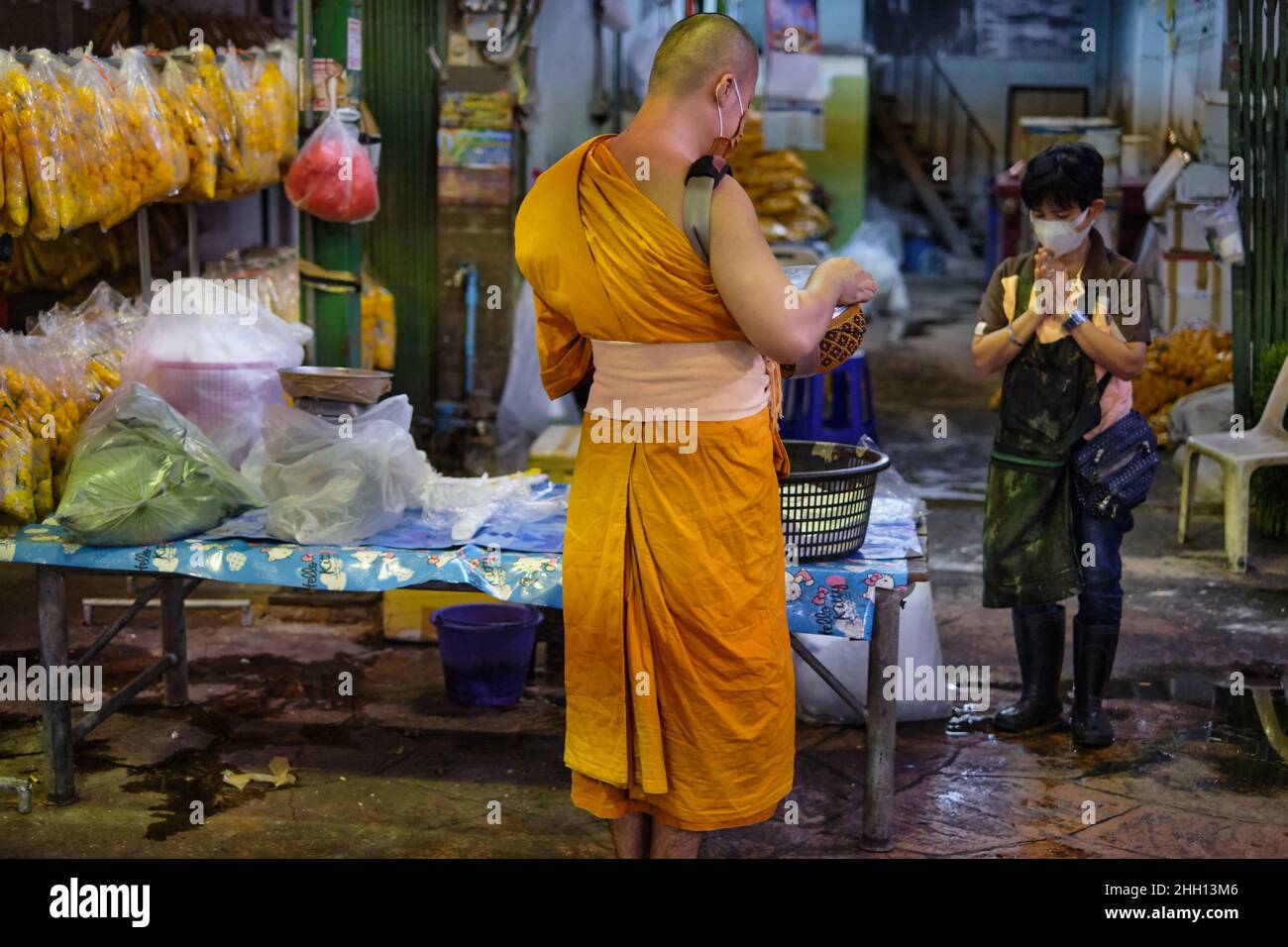 Während seiner gewöhnlichen Almosenrunde am Morgen wird ein thailändischer buddhistischer Mönch von einem Marktverkäufer mit einem wai (traditioneller thailändischer Gruß) begrüßt; Bangkok, Thailand Stockfoto