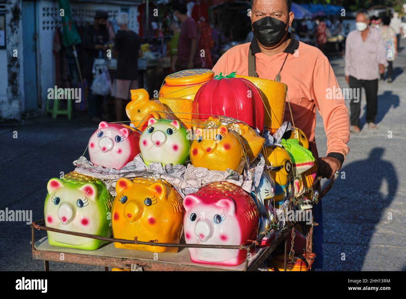 Ein thailändischer Straßenhändler schiebt seinen Wagen voller farbenfroher Sparschweine; Bangkok, Thailand Stockfoto