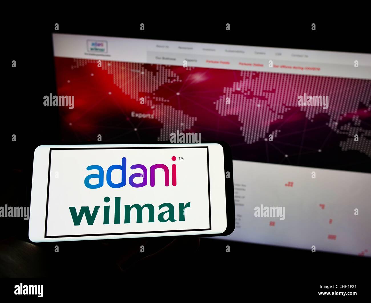 Person, die Mobiltelefon mit dem Logo des indischen Lebensmittelunternehmens Adani Wilmar Limited auf dem Bildschirm vor der Business-Webseite hält. Konzentrieren Sie sich auf die Telefonanzeige. Stockfoto