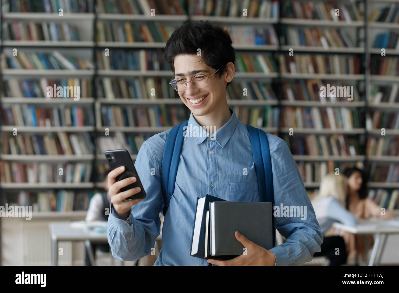 Aufgeregter junger Student in einer Brille mit gestapelten Büchern Stockfoto
