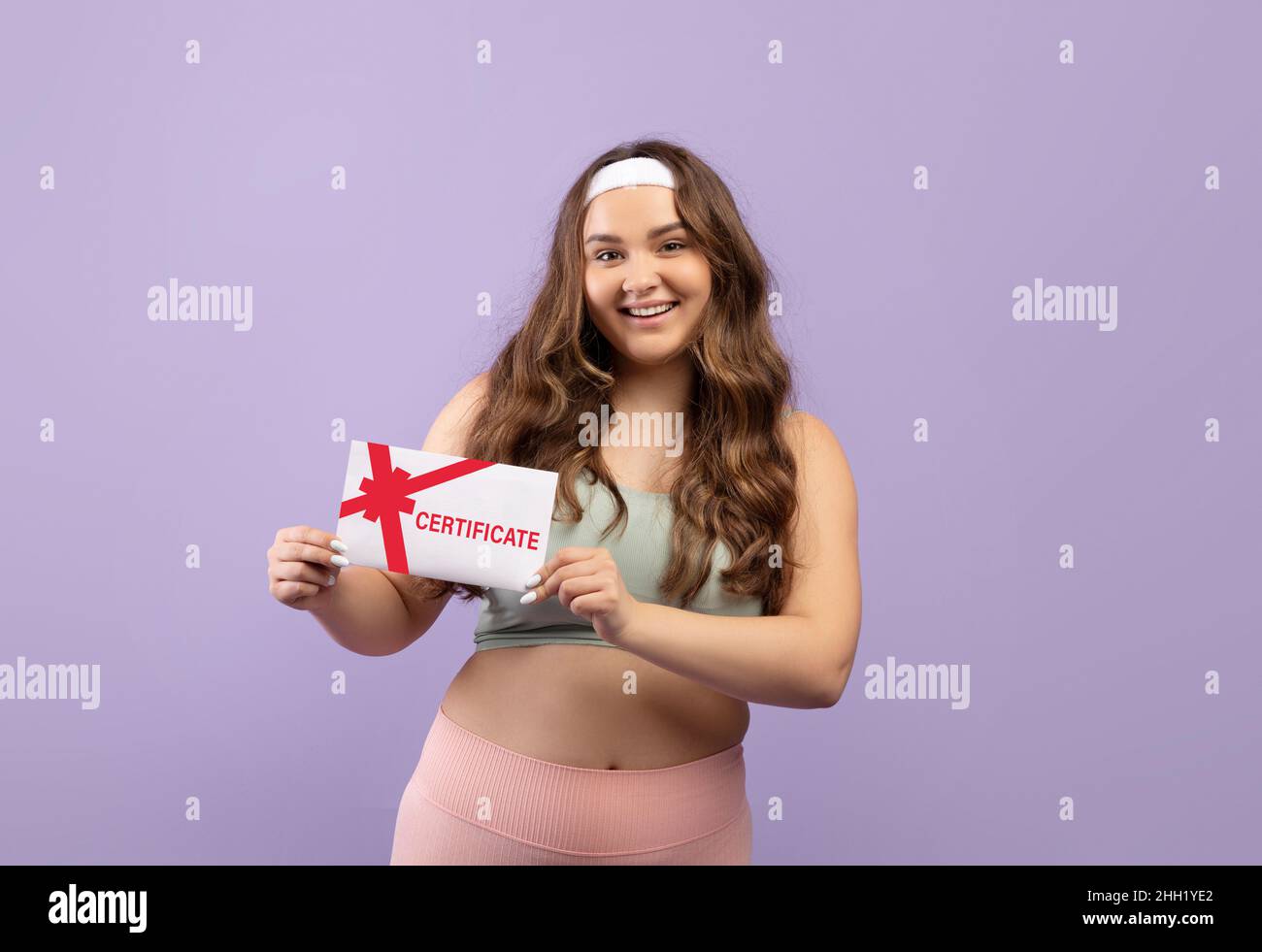 Fröhliche kaukasische junge Frau in Sportkleidung mit Geschenkgutschein für das Fitnessstudio Stockfoto