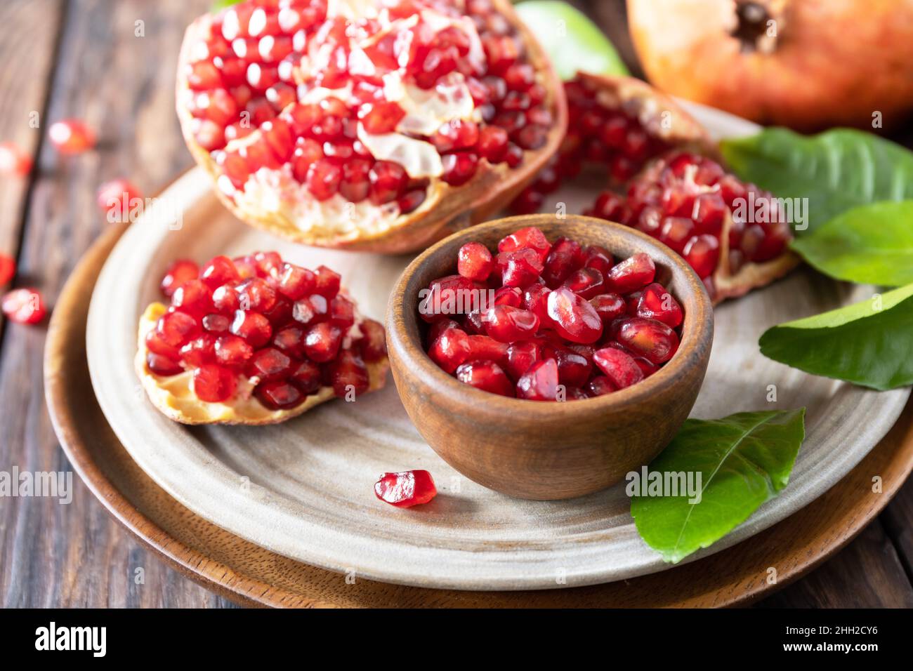 Reife saftige Granatapfelfrüchte in einer Holzschüssel auf einem rustikalen Tisch in der Nähe. Ernährung und gesunde Ernährung. Stockfoto