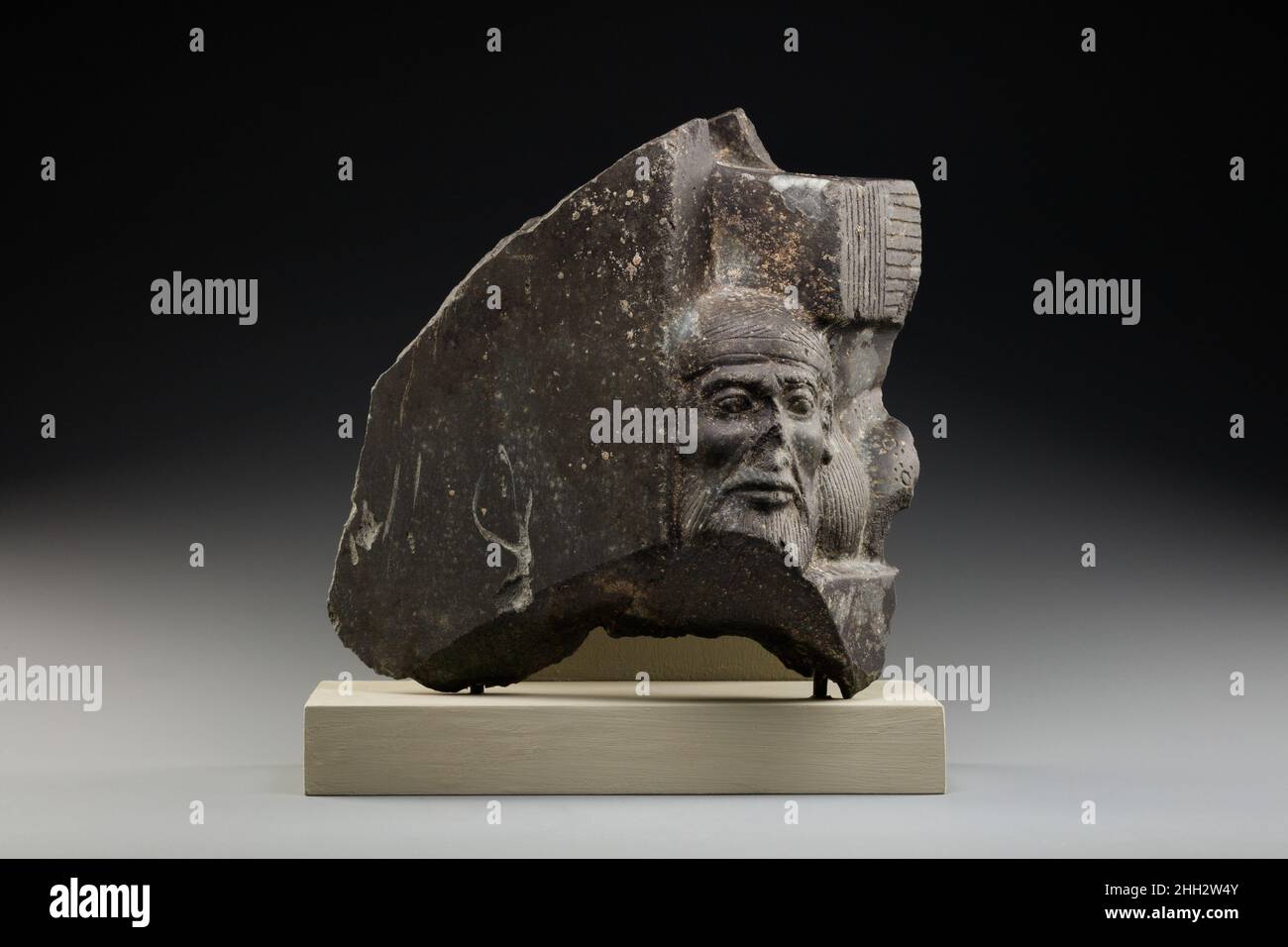 Fragment einer skulpturierten Statue, die einen asiatischen Gefangenen darstellt, ca. 1300–1250 v. Chr. Neues Königreich, Ramesside die Macht des pharao wurde von alten ägyptischen Künstlern durch eine Vielzahl von Bildern zum Ausdruck gebracht. Eines davon ist das Bild des pharao, der über den Leichen von ausländischen Gefangenen steht oder thront. Dieses Fragment eines Standbildes zeigt Kopf und Schulter eines Syrers, der durch lange Haarsträhnen gekennzeichnet ist, die von einem Stirnband, einem Bart und Schnurrbart und einem mit Rosetten bestickten Fransenmantel umrandet sind. Die komplette Figur lag flach auf seinem Bauch, sein Rücken durch die Schilfmatte gedrückt, auf der Stockfoto