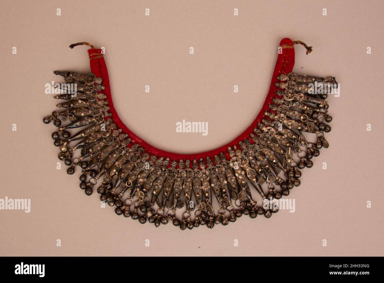 Halskette 19th Jahrhundert Halsketten mit mehreren Anhängern, die in Glocken enden, sind bei beduinischem Frauenschmuck aus der zentralen Region Saudi-Arabiens recht häufig. Die auditive Wirkung dieser dutzenden Glocken, die sich im Gleichklang bewegen, erzeugt einen großartigen Klang, während sich der Träger bewegt. Halsketten wie diese waren Wunder für die Ohren und die Augen. Silber war das bevorzugte Material für Beduinenjuwelen, und dieses Beispiel zeigt auch die Vorliebe für Rückenjuwelen auf einem roten Stoff, auf dem die Anhänger vernäht sind. Halskette. 19th Jahrhundert. Silber und Stoff. Saudi-Arabien zugeschrieben. Stockfoto