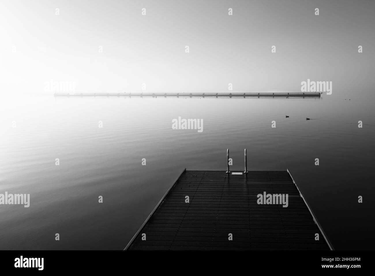 Dämmerung auf einem Holzsteg Stretching in den stillen Ozean in beeindruckenden Schwarz und Weiß Stockfoto