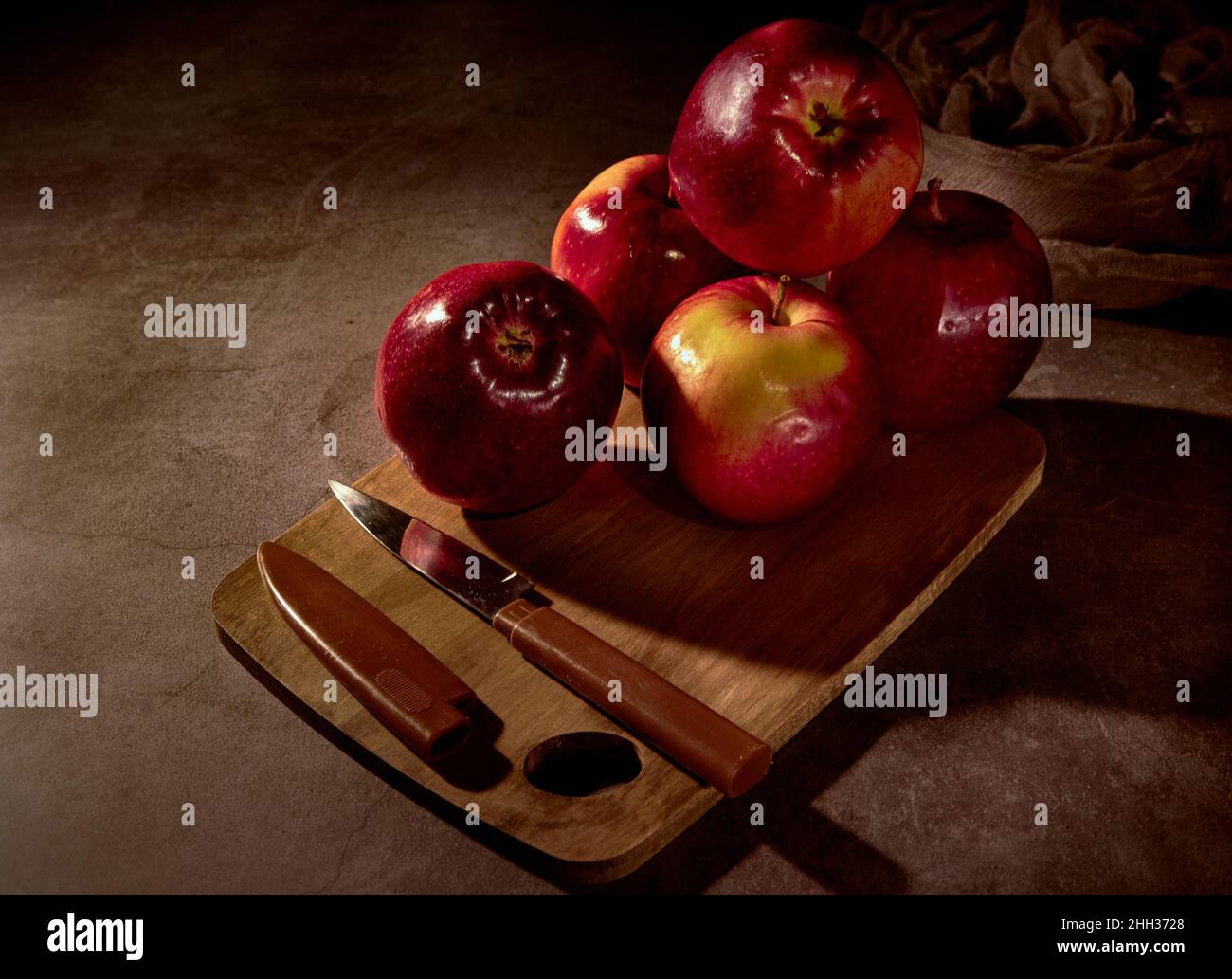Apfelbrett. Äpfel und ein Messer stehen auf einem Schneidebrett und die ganze Komposition hat einen dunklen Hintergrund. Stockfoto