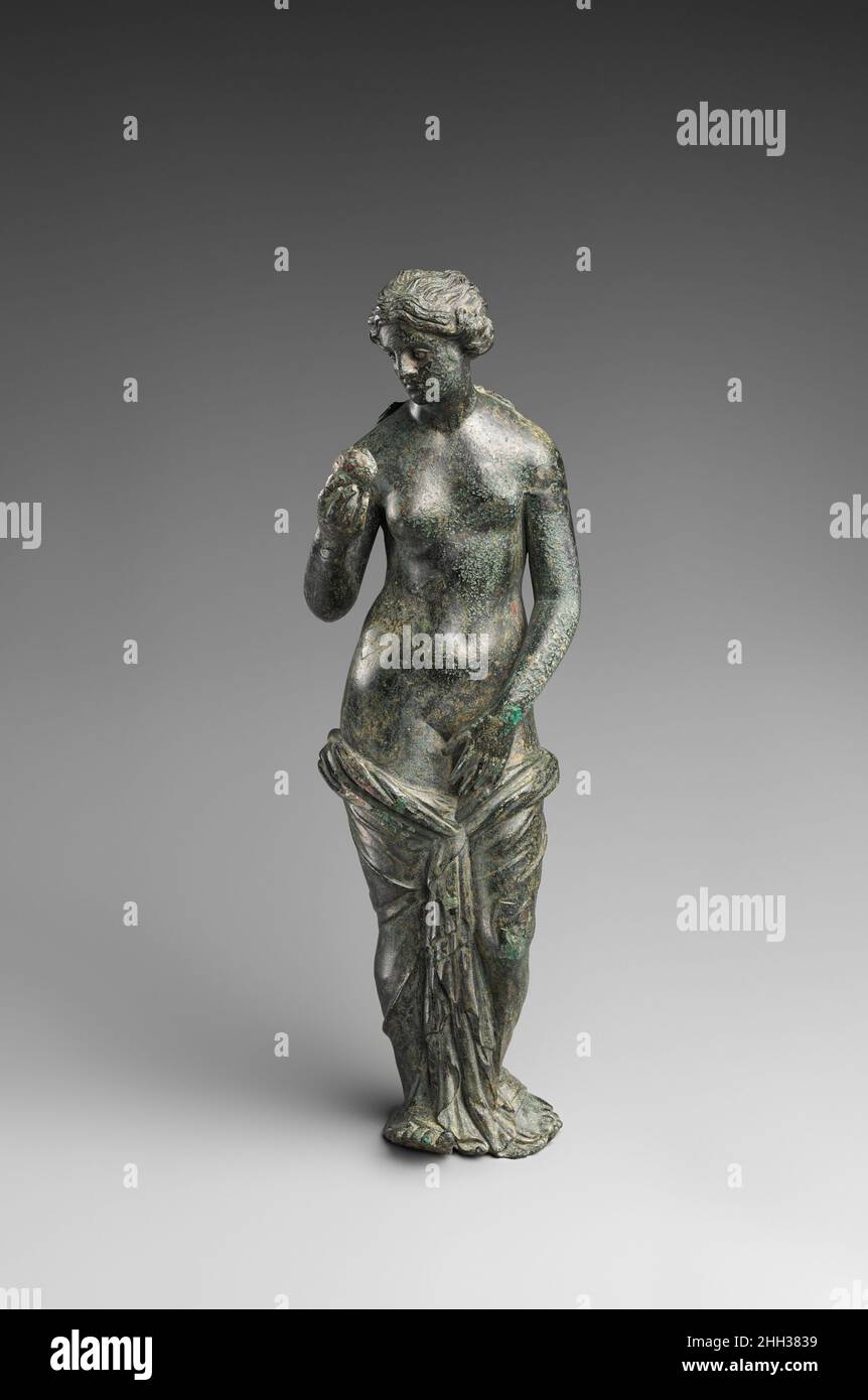 Bronzestatuette der Aphrodite mit silbernen Augen 3rd–1st Jahrhundert v. Chr. die griechische Aphrodite hält in Kontemplation den Apfel hoch, den ihr der trojanische Prinz Paris als Preis für die schönste der griechischen Göttinnen gegeben hat. Dieses eindringliche Bild verstärkt diese Unterscheidung, erinnert aber auch an die Ursache des Trojanischen Krieges. Als Gegenleistung für den Apfel bot Aphrodite Paris die schönste Frau der Welt an, Helen, die Frau des griechischen Königs Menelaos. In der klassischen griechischen Kunst illustrieren Szenen des Mythos nicht den Apfel, der zuerst in der hellenistischen Periode erschien. Bronzestatuette der Aphrodite mit Stockfoto