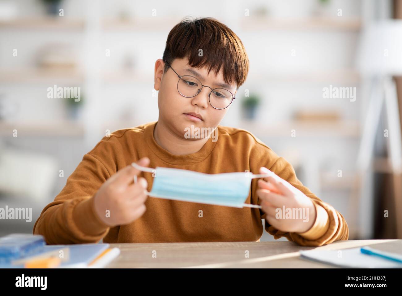 Gelangweilt asiatische teen junge halten schützende Gesichtsmaske Stockfoto