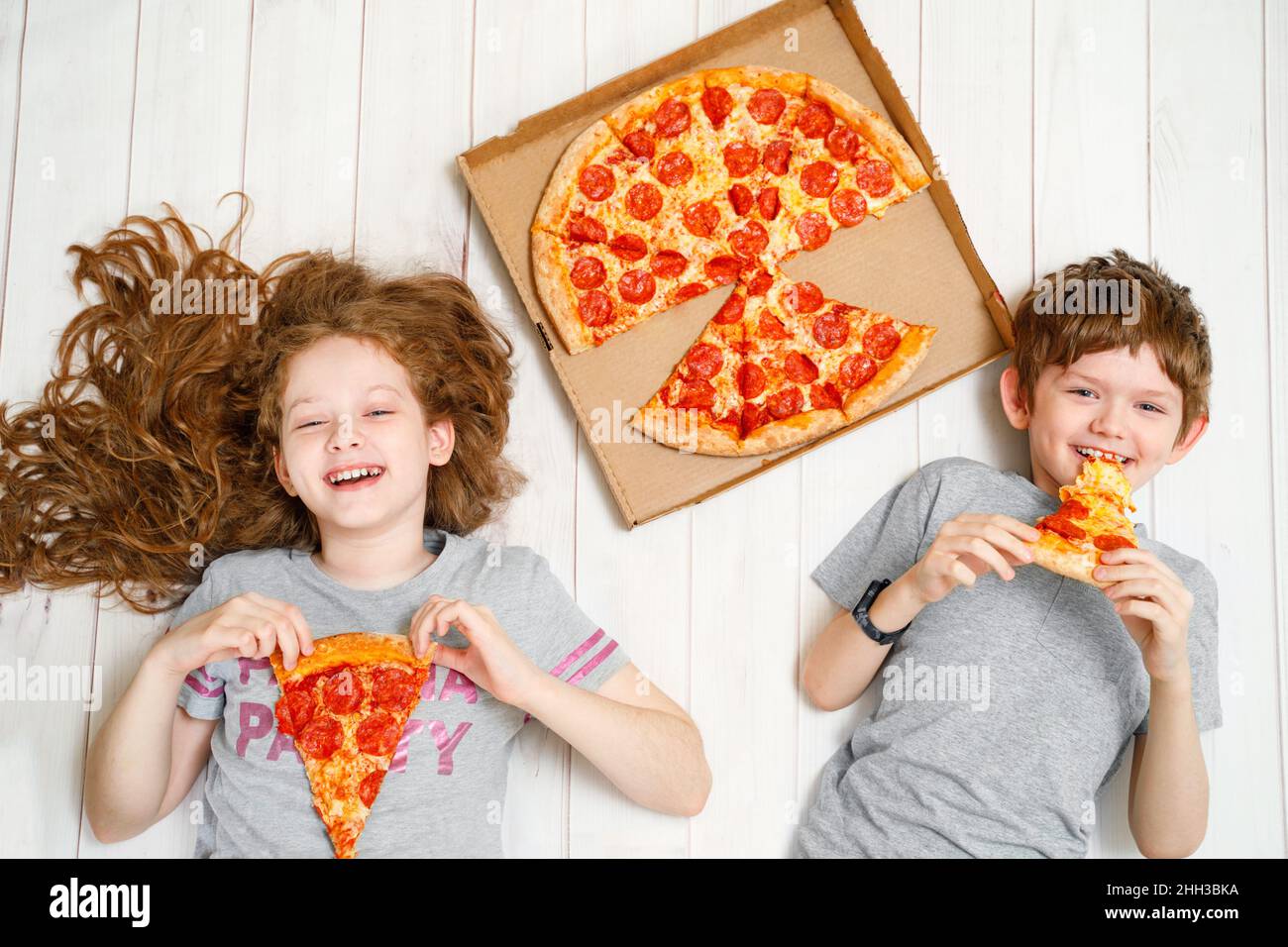 Kinder, die eine Pizza auf dem Holzboden halten. Quarantänefeier zu Hause. Stockfoto