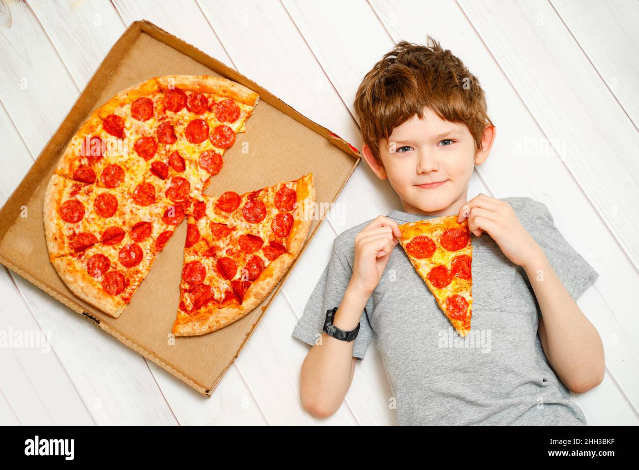 Niedliches Kind, das eine Pizza auf dem Holzboden hält. Quarantänefeier zu Hause. Stockfoto