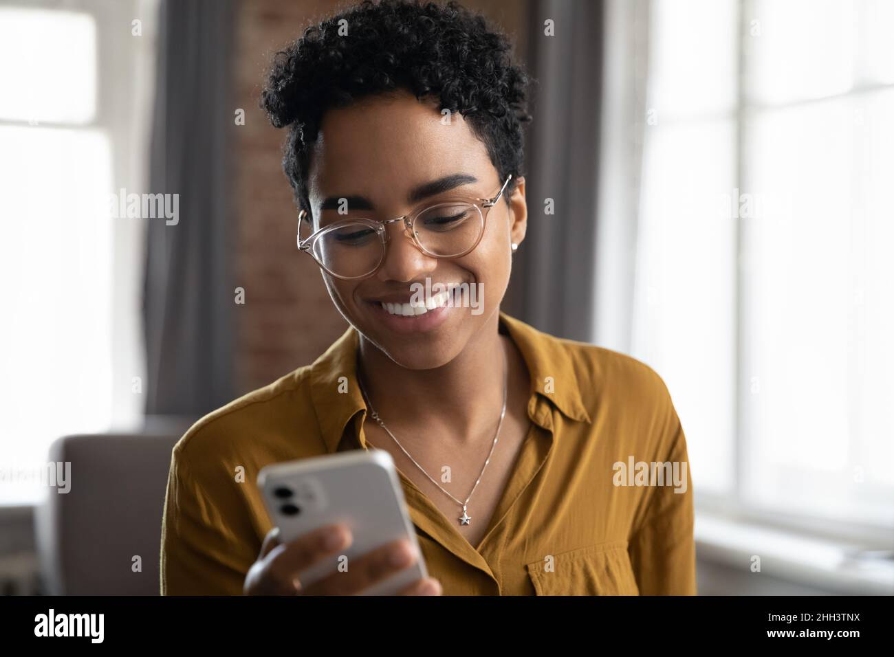 Glückliche Afro-amerikanische junge Geschäftsfrau in Brille mit Smartphone Stockfoto